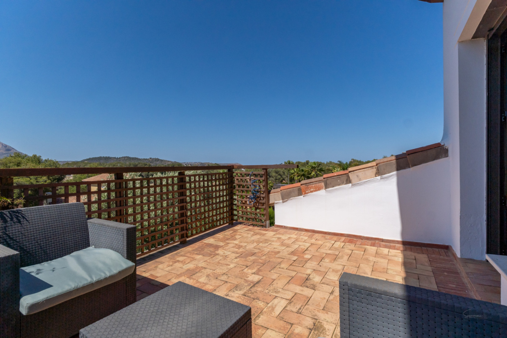 Private Dachterrasse mit Terrakotta-Fliesen, grauen Korbmöbeln und Holzgitter-Geländer mit weitem Blick über die Hügellandschaft.