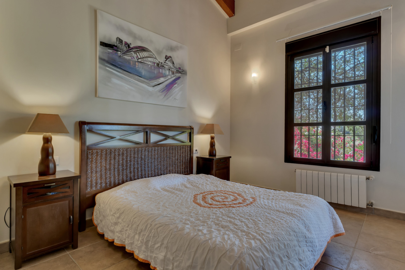 Schlafzimmer mit dunklem Holzbett und geflochtenem Kopfteil, passenden Nachttischen, hohen Decken mit Holzbalken und Blick in den Garten.