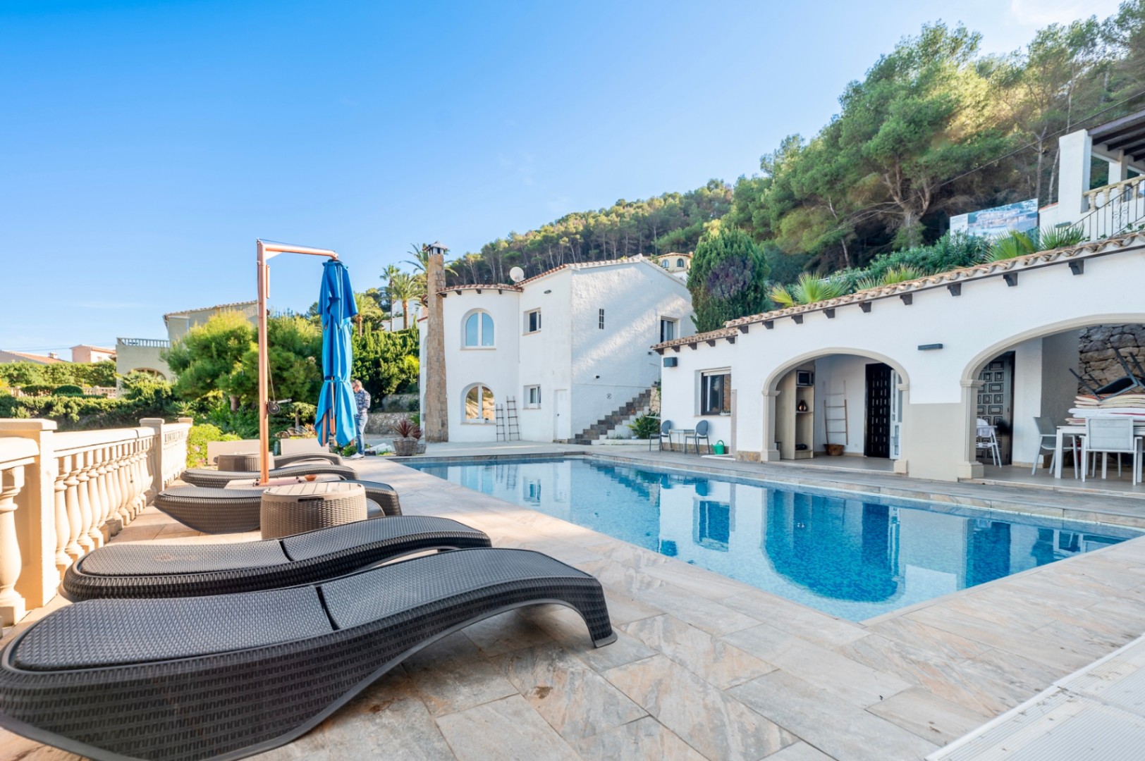 Außenbereich mit rechteckigem Pool, ergonomischen Sonnenliegen und traditionellen Rundbogen-Veranden vor der weißen Fassade der Villa.