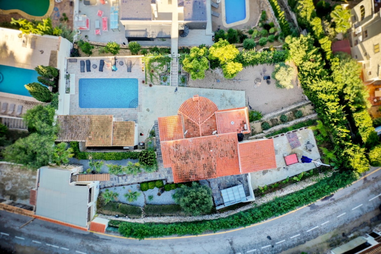 Luftaufnahme der Villa, die die Grundstücksaufteilung, den rechteckigen Pool mit Steinterrasse und das traditionelle Ziegeldach zeigt.