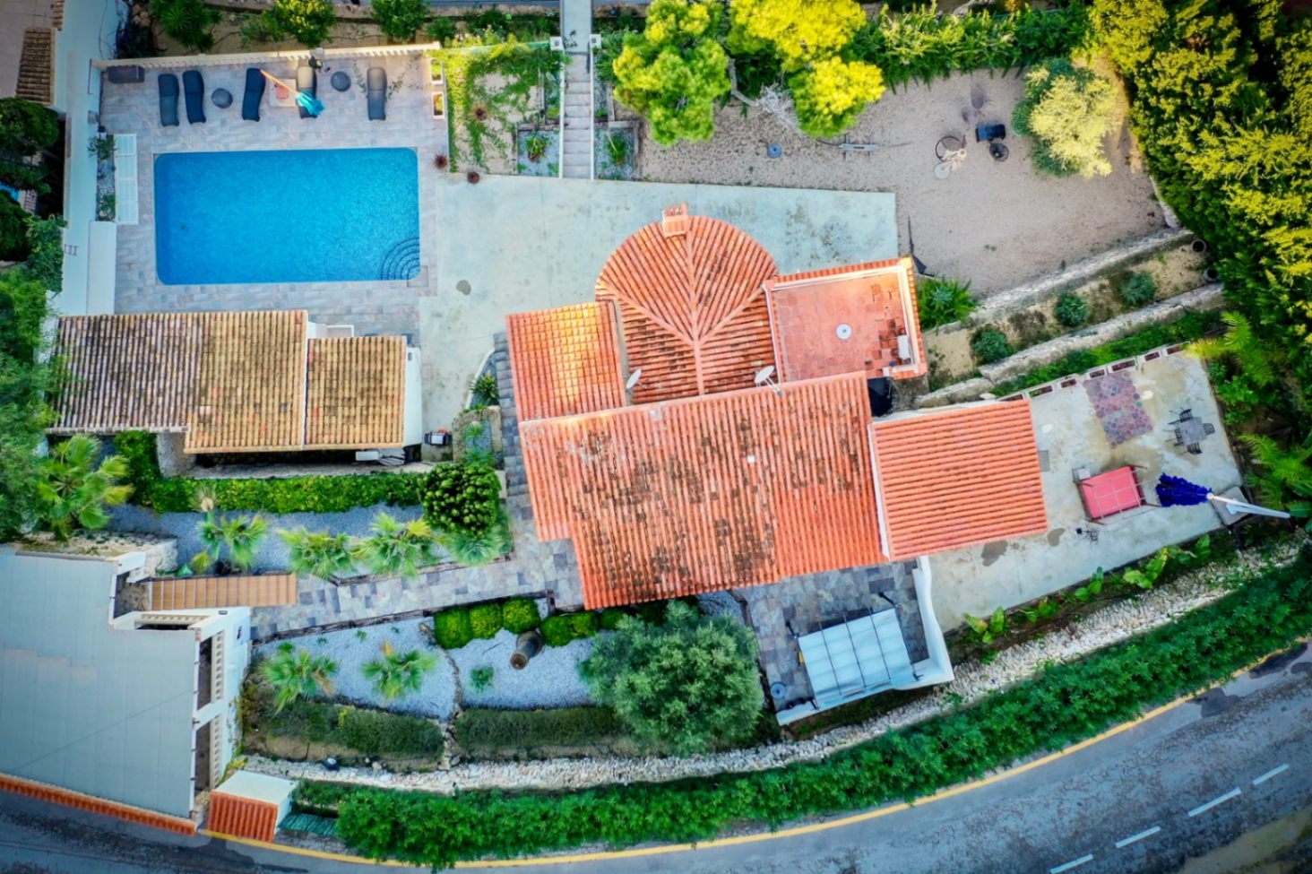Luftaufnahme der Villa mit Blick auf das Terrakottadach, den rechteckigen Pool mit Sonnenterrasse und die mediterran gestaltete Gartenanlage mit Steinwegen.