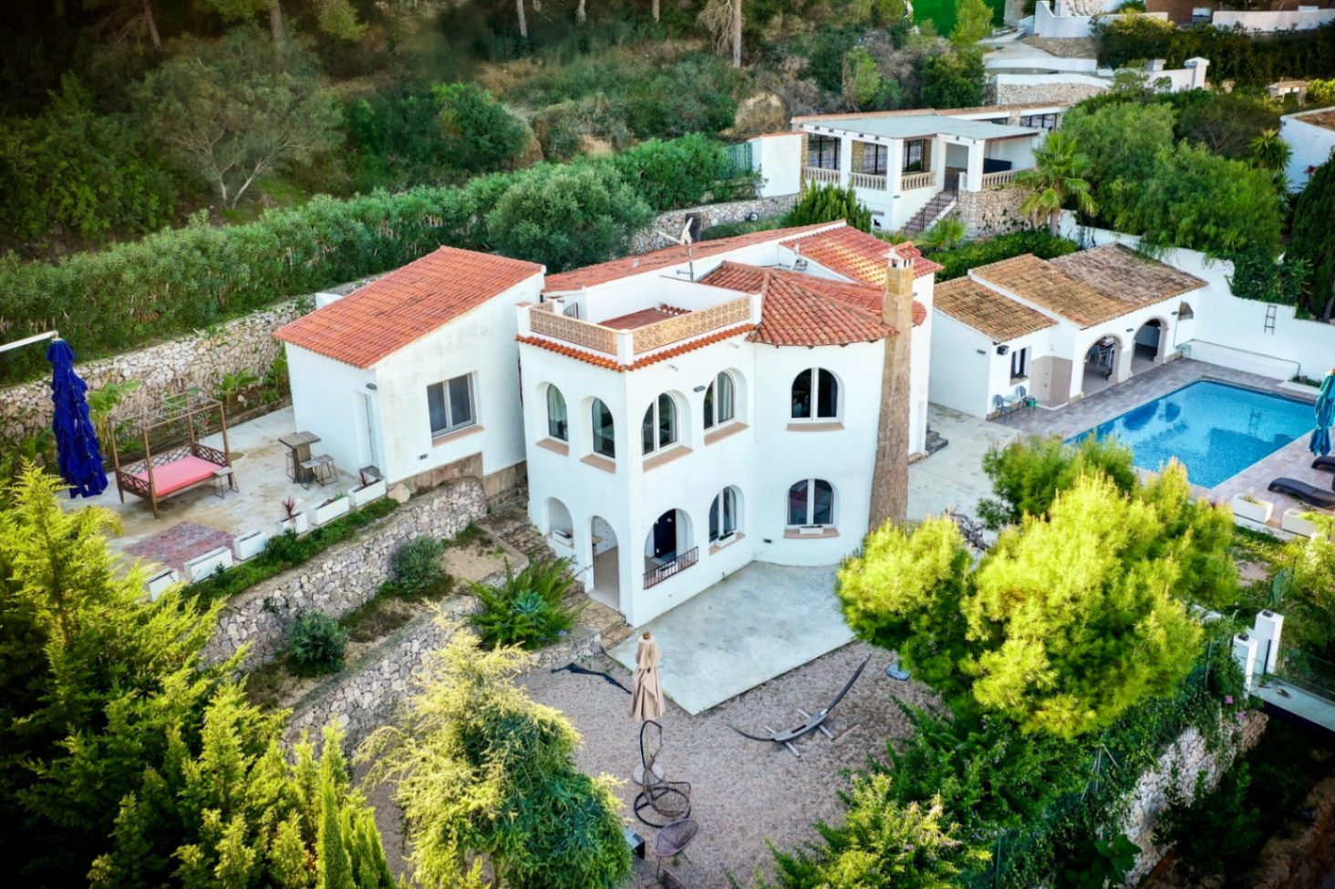 Luftaufnahme der Villa mit weißer Fassade, Rundbogenfenstern und Ziegeldächern, eingebettet in terrassierte Steingärten mit privatem Poolbereich.