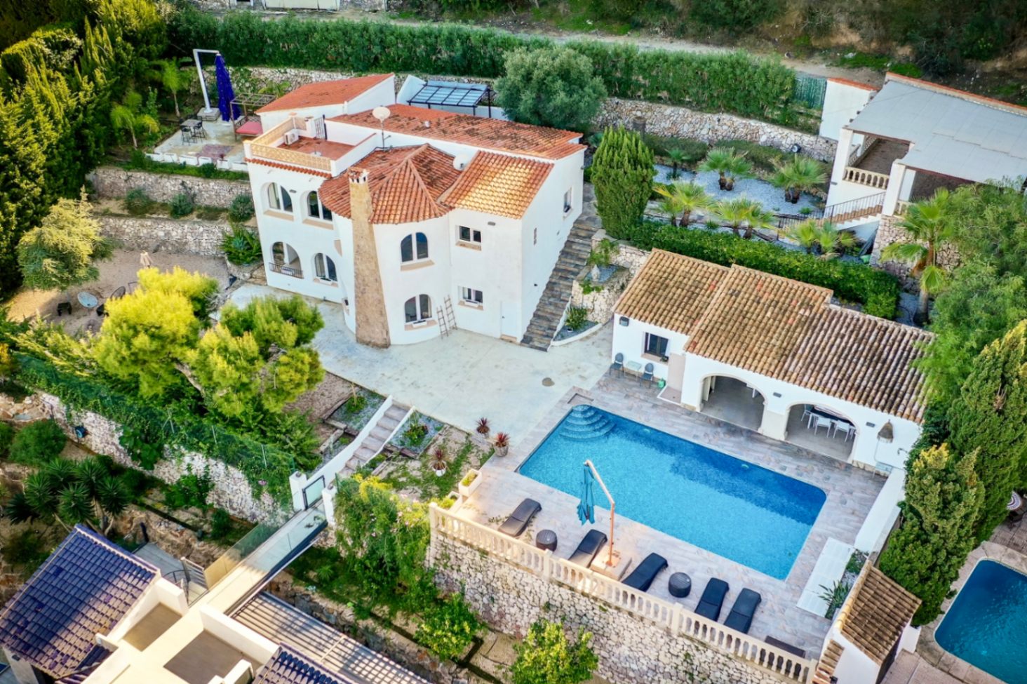 Luftaufnahme der weißen Villa mit Terrakottadach, rechteckigem Pool, Steinterrasse und terrassierten Gärten mit Natursteinmauern in Portitxol.