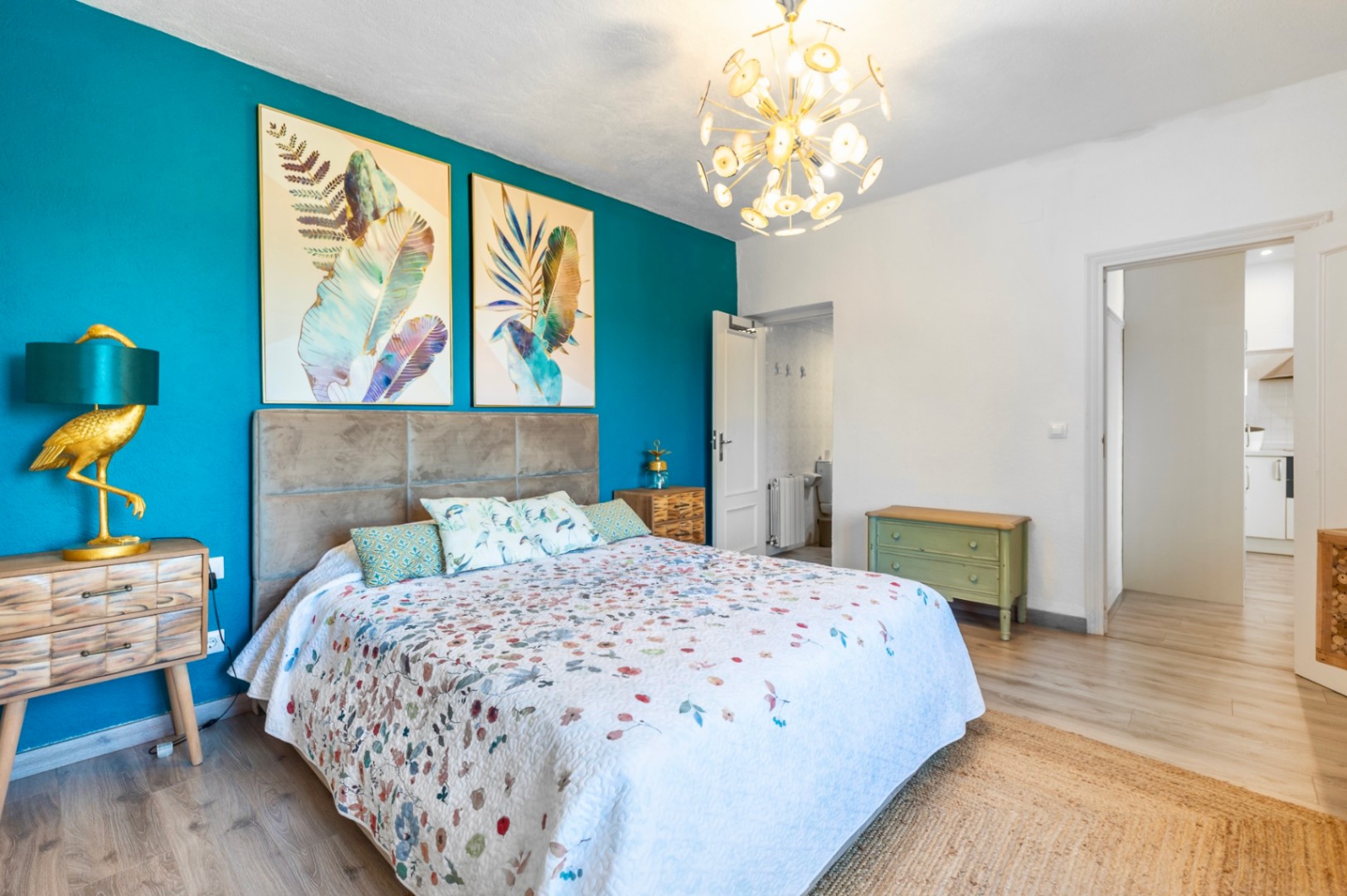 Schlafzimmer mit türkisfarbener Akzentwand, gepolstertem Kopfteil und Sputnik-Kronleuchter. Es bietet ein En-Suite-Bad und hellen Laminatboden in Holzoptik.