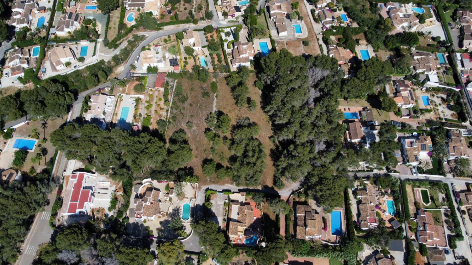 Luftaufnahme des weitläufigen, flachen Grundstücks in einem etablierten Wohngebiet mit Villen, Pools und mediterranem Baumbestand.