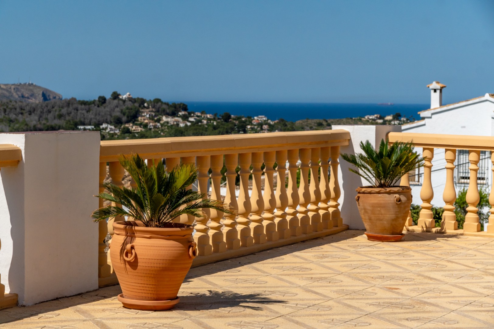 Erhöhte Terrasse mit gemusterten Bodenfliesen, klassischer Balustrade und Terrakotta-Pflanzgefäßen mit weitem Blick auf das Mittelmeer und die Küste.