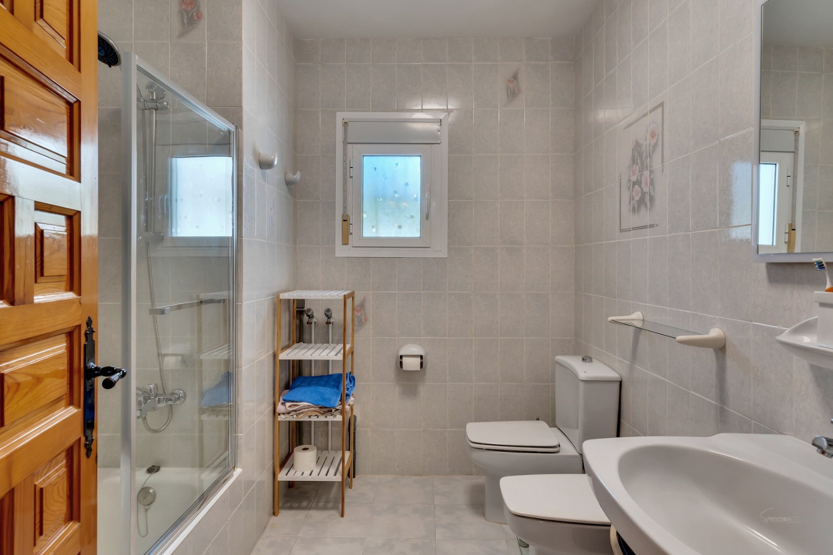Funktionales Badezimmer mit Glasduschkabine, weißen Sanitäranlagen und gefliesten Wänden. Es verfügt über ein Fenster für Tageslicht und eine Massivholztür.