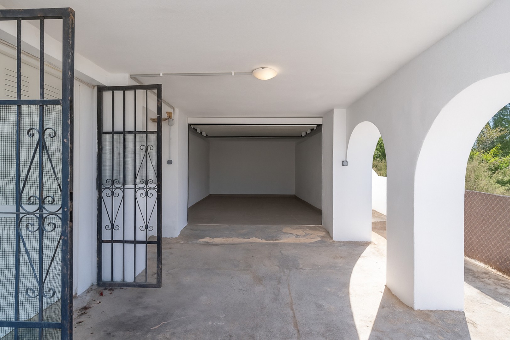 Geschlossene Garage und überdachter Parkplatz mit mediterranen Rundbögen, weißen Wänden und einem schwarzen schmiedeeisernen Sicherheitstor.