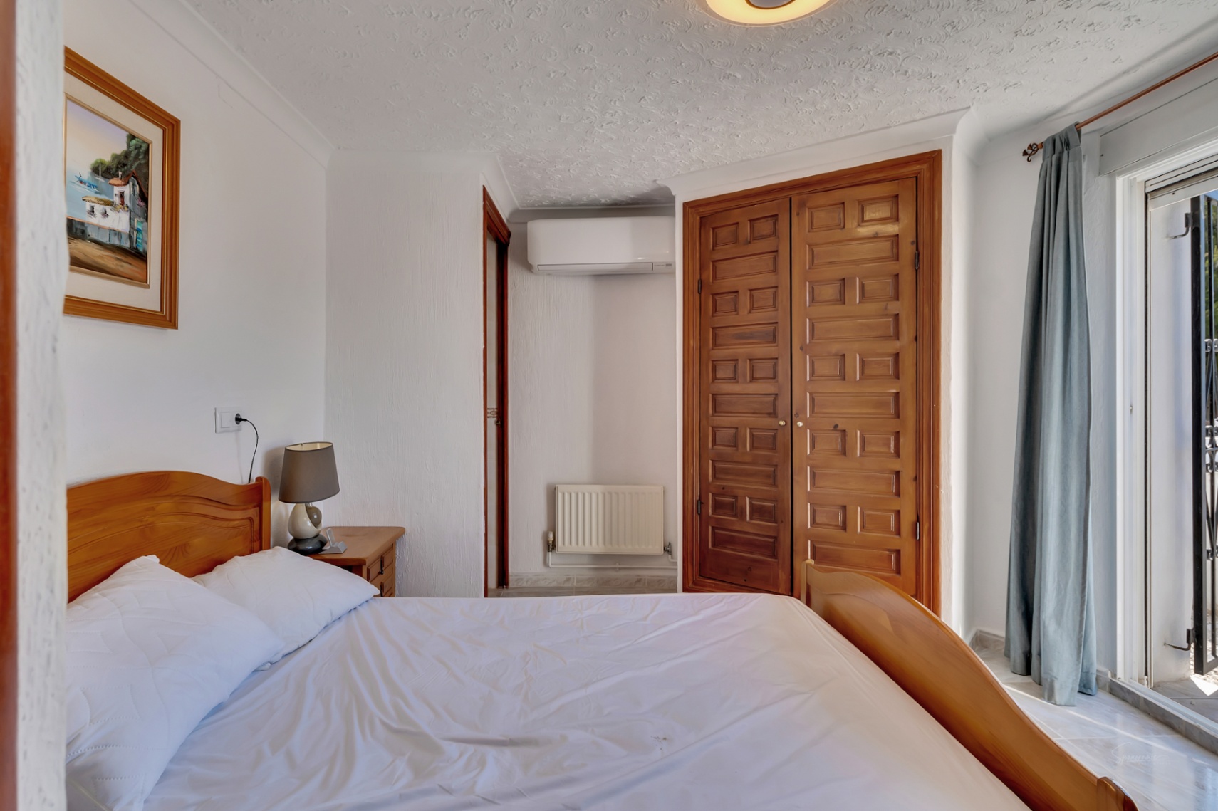 Helles Schlafzimmer mit geschnitztem Einbauschrank aus Holz, Klimaanlage und direktem Zugang zur Terrasse durch Glasschiebetüren.