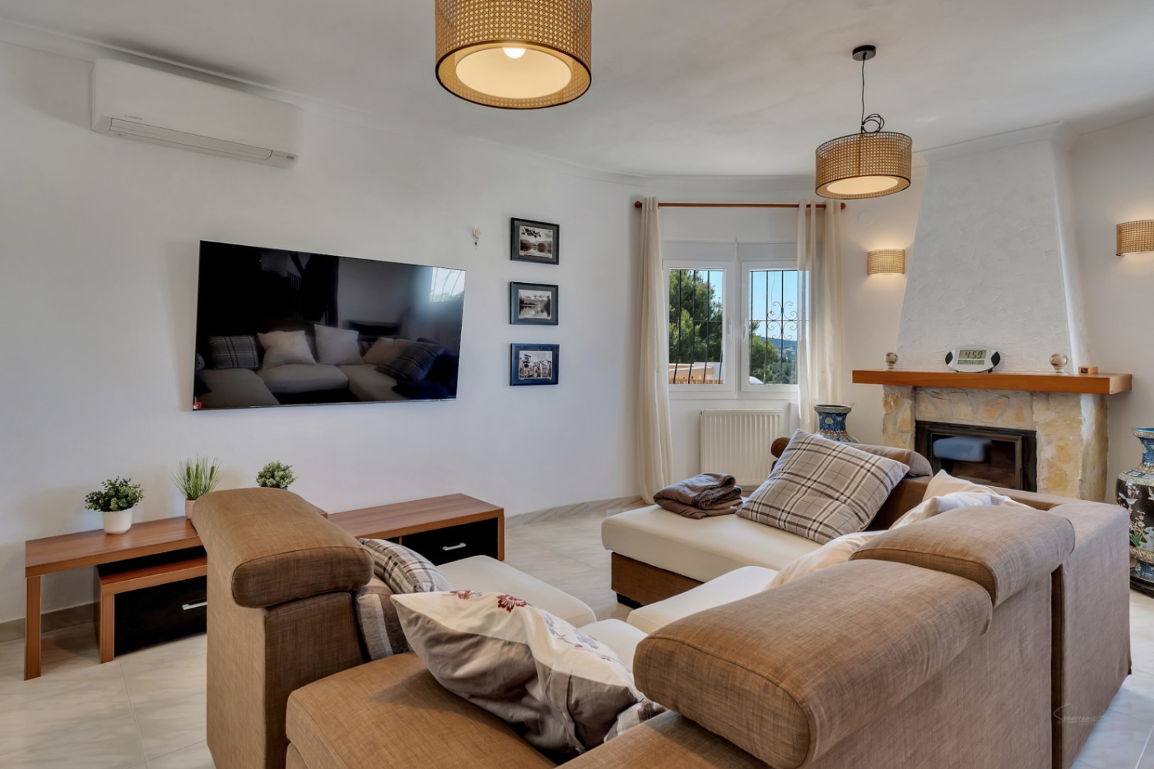 Helles Wohnzimmer mit Naturstein-Kamin, Klimaanlage und dekorativen Rattan-Leuchten. Ausgestattet mit einem großzügigen Ecksofa und wandmontiertem TV.