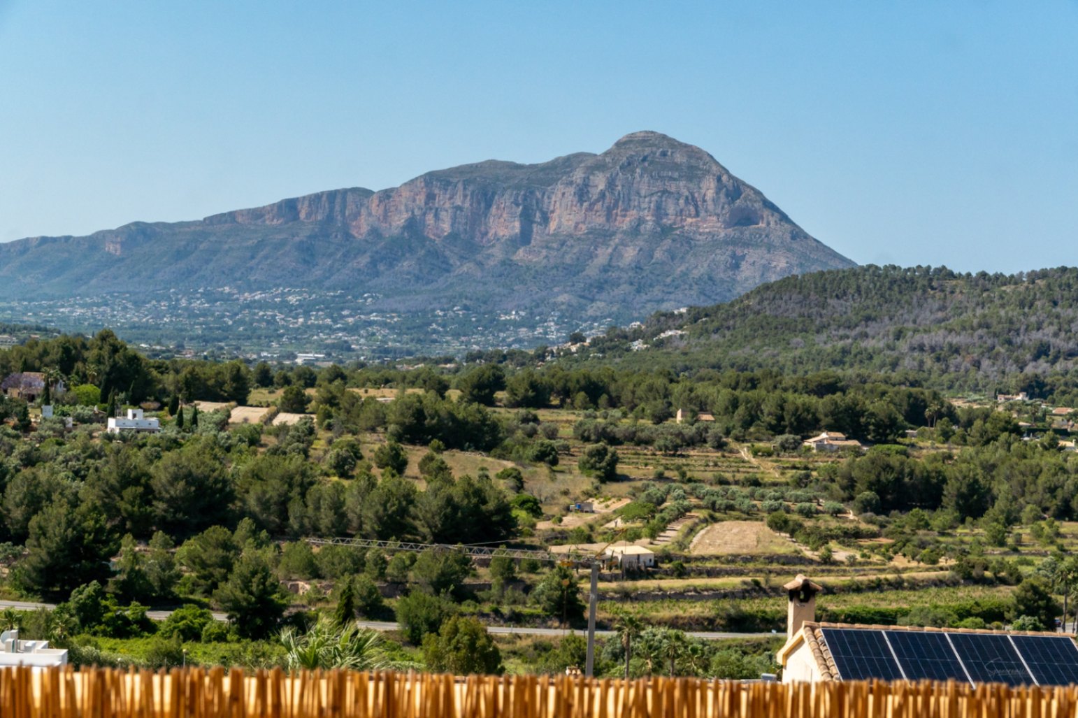Panoramablick auf das Montgó-Massiv über ein grünes Tal mit mediterraner Vegetation und Hausdächern, die mit Photovoltaikanlagen ausgestattet sind.
