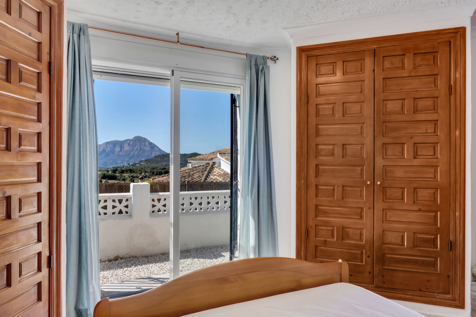 Schlafzimmer mit Einbauschrank aus Holz und direktem Zugang zur Terrasse mit Panoramablick auf den Berg Montgó.