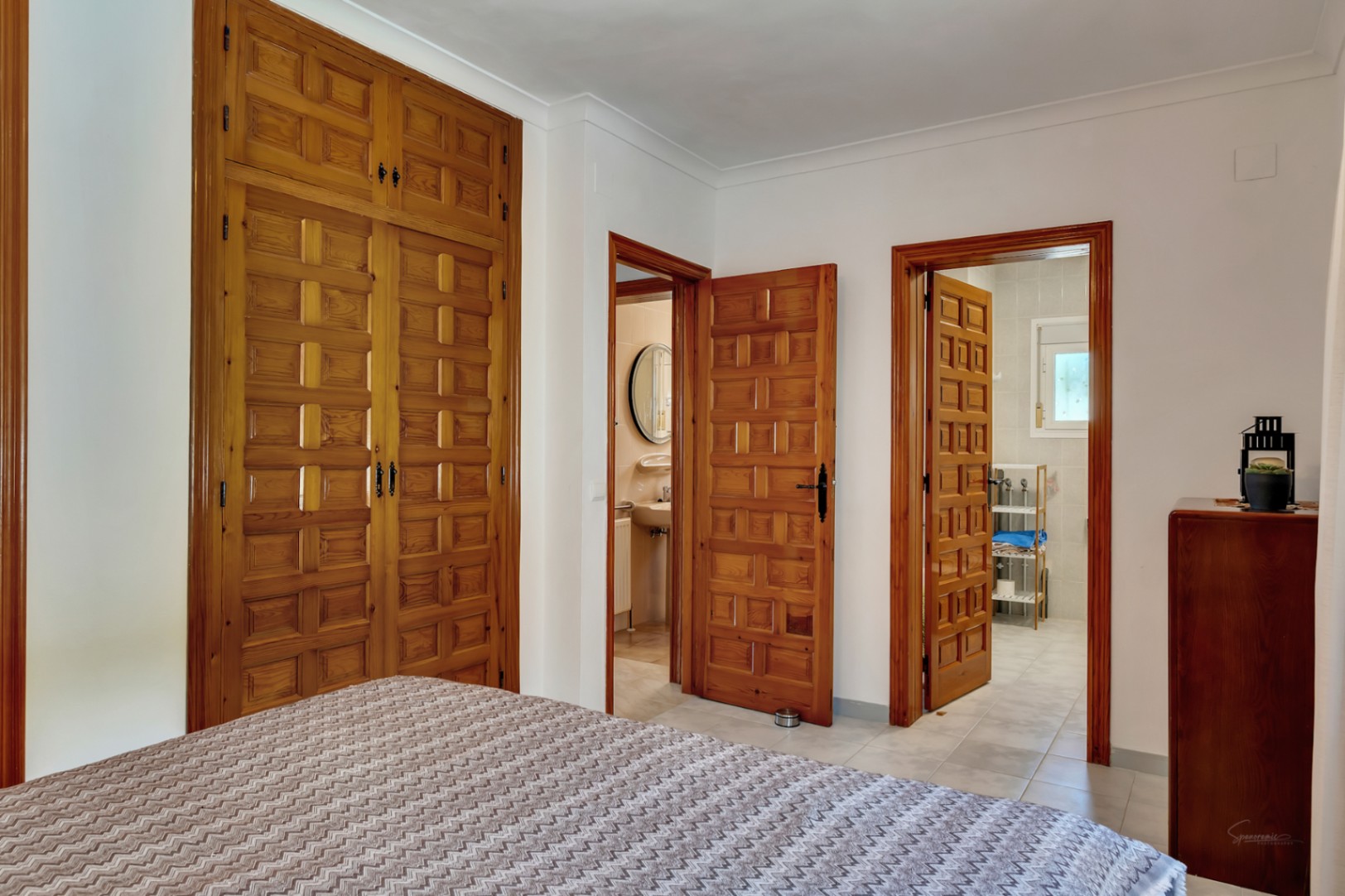 Schlafzimmer mit maßgefertigten Einbauschränken aus geschnitztem Holz und Zugang zu zwei En-Suite-Bädern, geprägt von traditioneller Handwerkskunst.