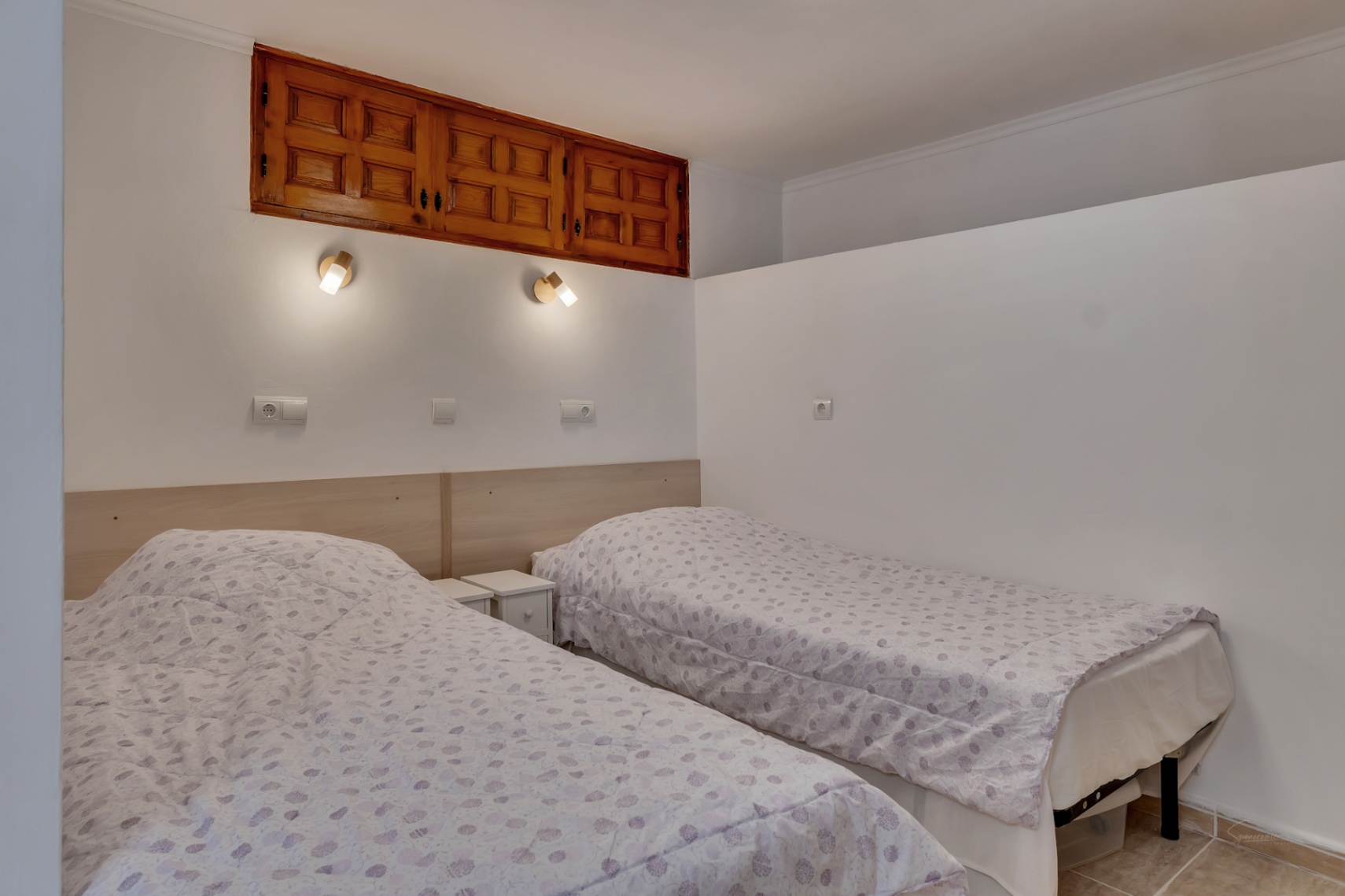 Schlafzimmer mit zwei Einzelbetten, hellem Holzkopfteil und traditionellen Einbauschränken aus Holz über den wandmontierten Leselampen.
