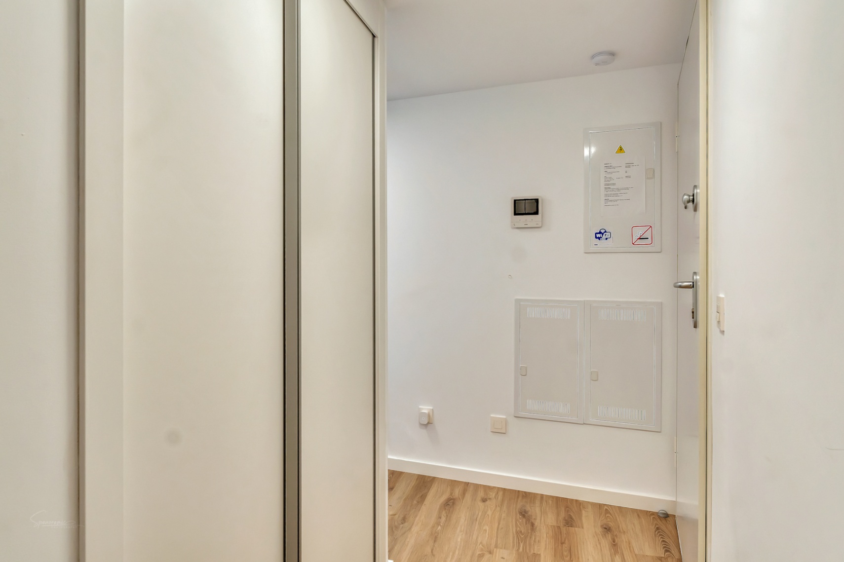 Eingangsbereich mit hellem Holzboden, großem weißem Einbauschrank und integrierten Bedienfeldern für die Haustechnik und Video-Gegensprechanlage.