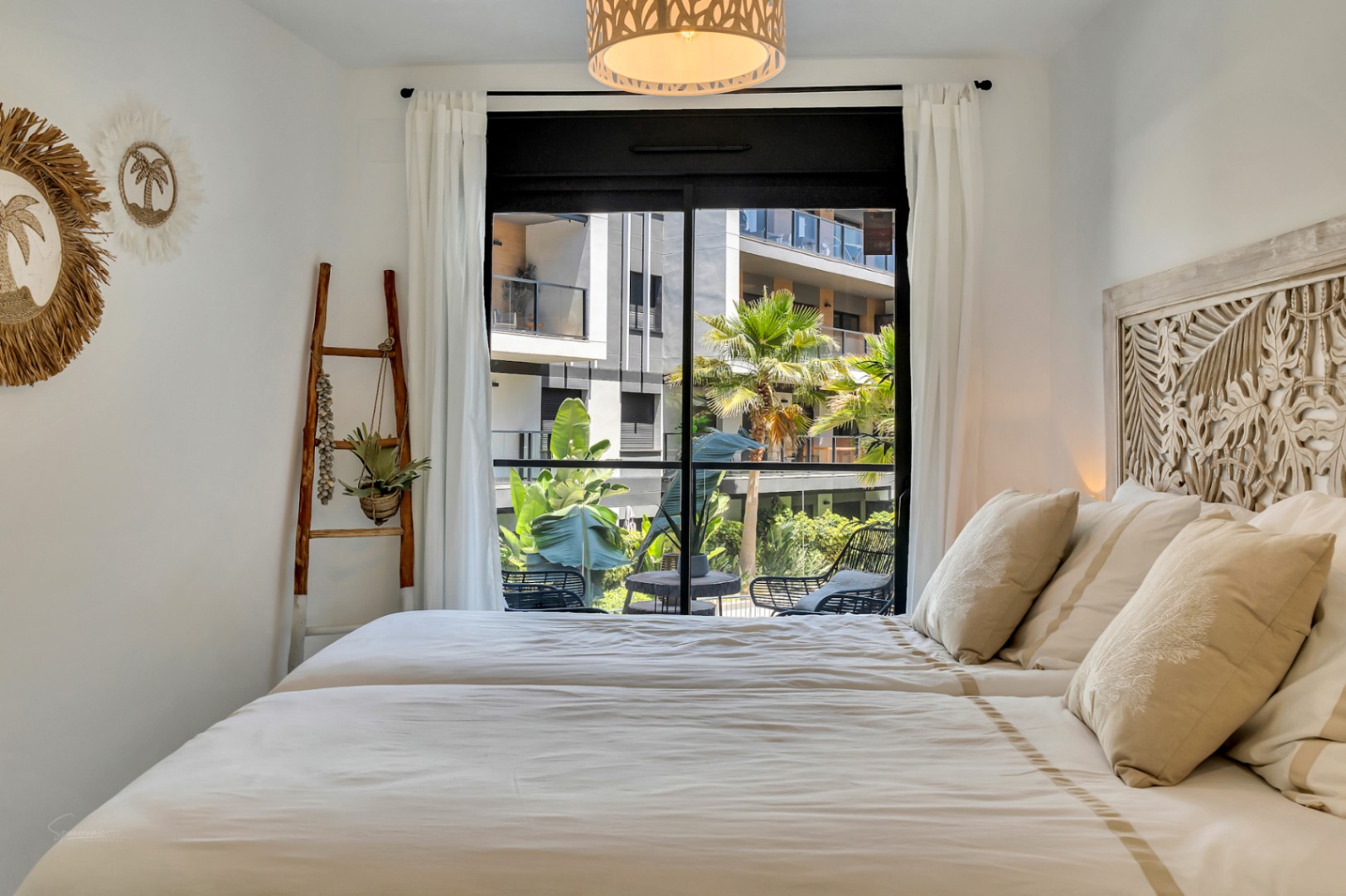 Helles Schlafzimmer mit kunstvoll geschnitztem Holzkopfteil, mediterranem Dekor und direktem Zugang zur privaten Terrasse mit Blick auf die Gemeinschaftsanlage.