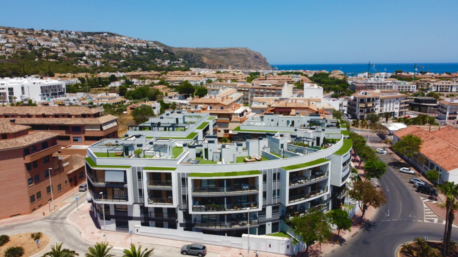 Luftaufnahme der modernen Wohnanlage in Jávea mit geschwungener Architektur, Dachterrassen mit Kunstrasen und Panoramablick auf das Mittelmeer.