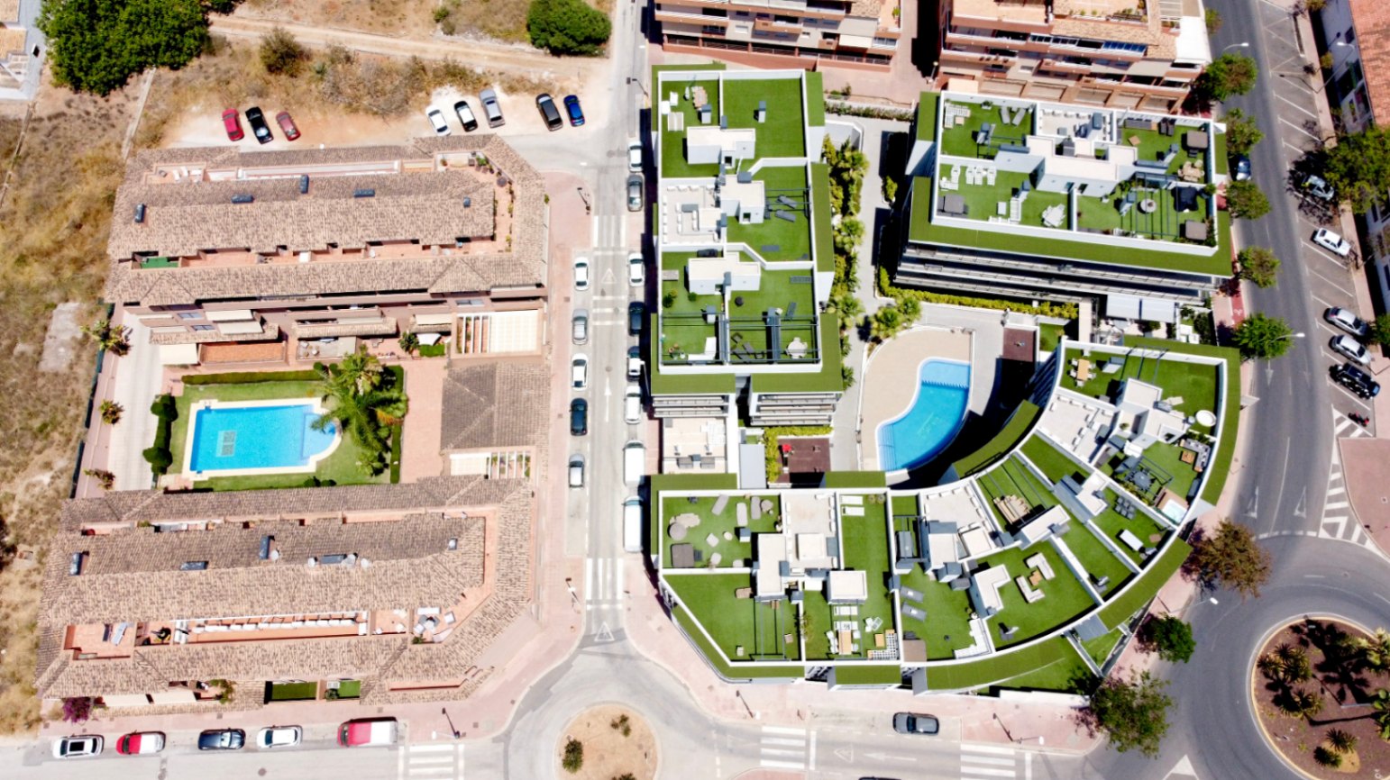 Luftaufnahme der modernen Wohnanlage mit begrünten Dachterrassen, zeitgenössischer Architektur und einem zentralen, geschwungenen Gemeinschaftspool.