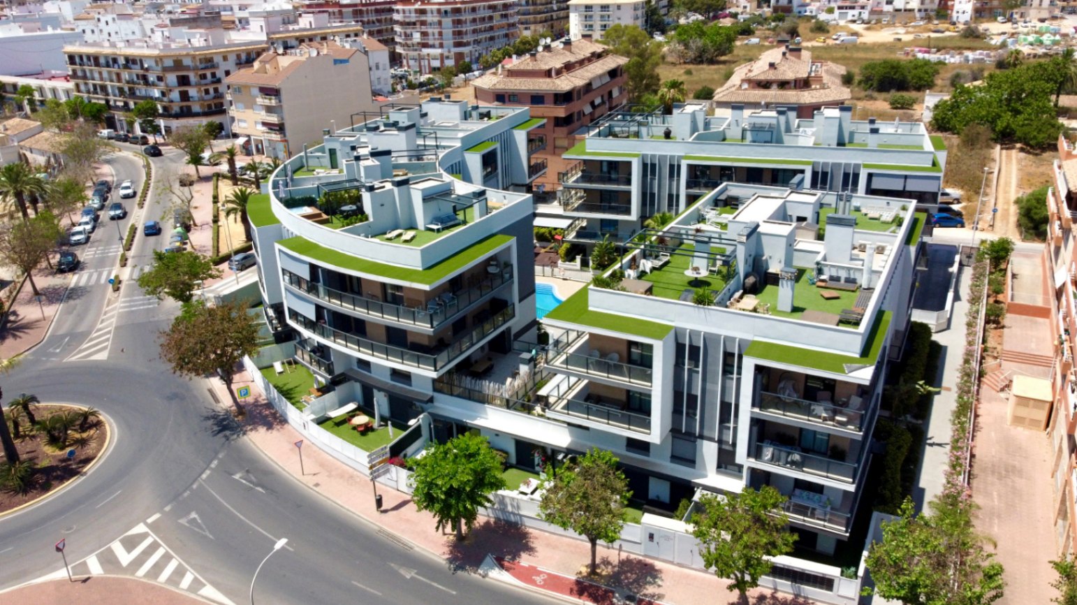 Luftaufnahme einer modernen Wohnanlage in Jávea mit geschwungenen Fassaden, großzügigen Dachterrassen mit Kunstrasen und einem zentralen Gemeinschaftspool.
