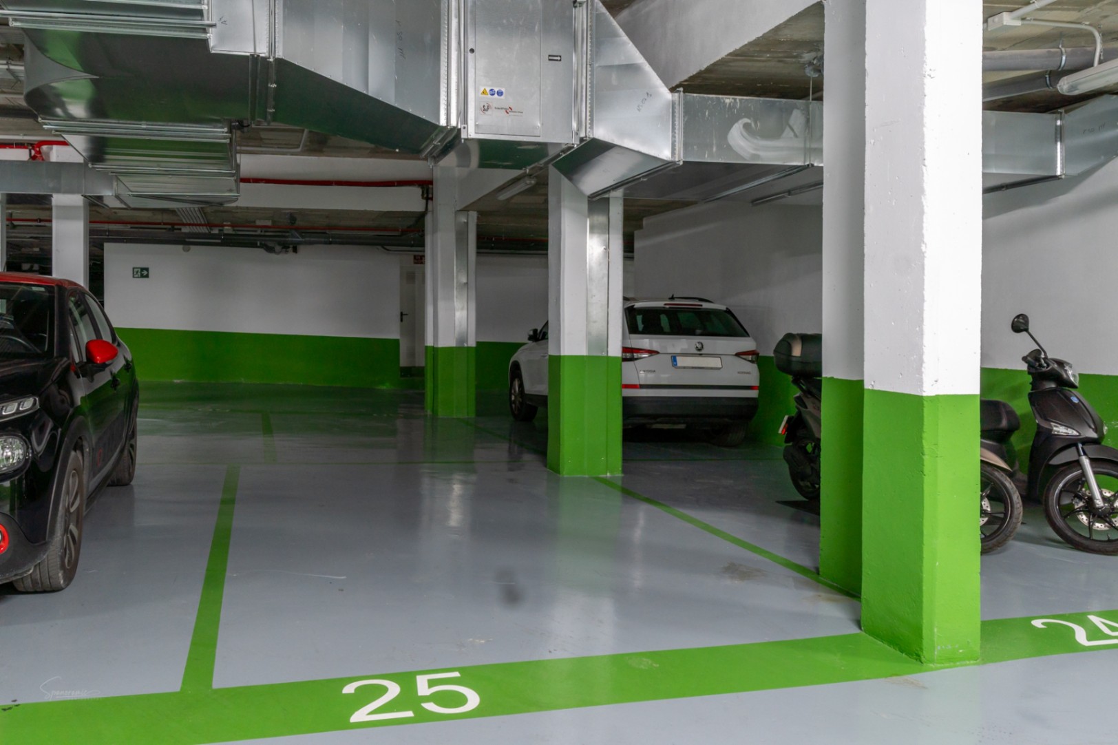 Nummerierter Tiefgaragenstellplatz mit grauem Epoxidharzboden und grünen Markierungen. Sichtbare Lüftungsrohre und Betonpfeiler prägen den modernen Raum.