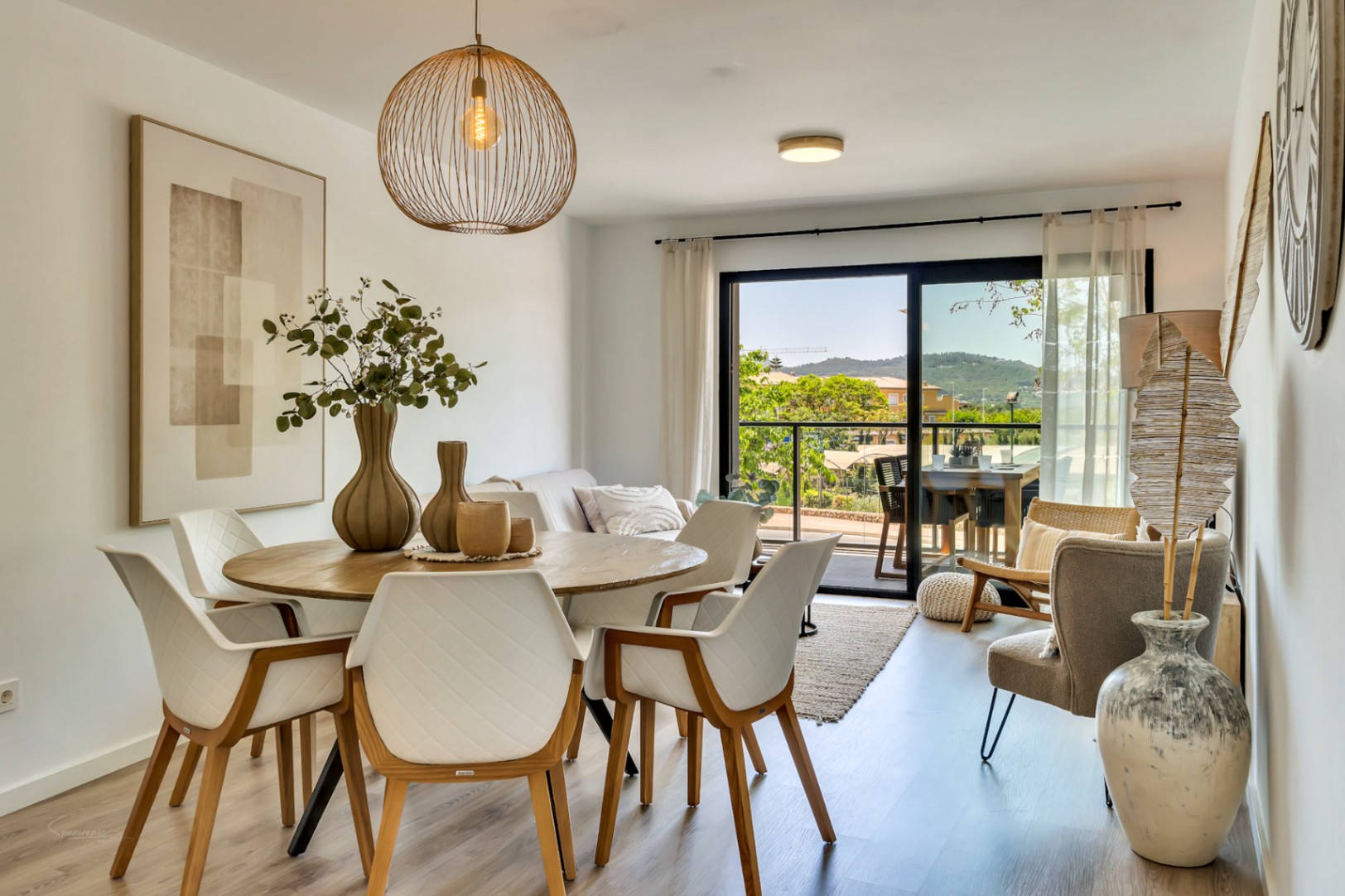 Offener Wohn- und Essbereich mit rundem Holztisch, stilvoller Pendelleuchte und großen Glasschiebetüren, die auf eine Terrasse mit Bergblick führen.