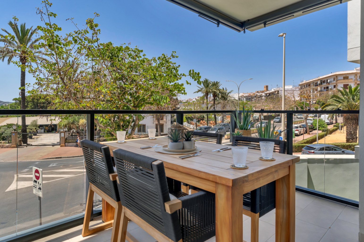 Private Terrasse mit Esstisch aus Holz, geflochtenen Stühlen und Glasgeländer, die einen freien Blick auf die umliegende Stadtlandschaft und Palmen bietet.