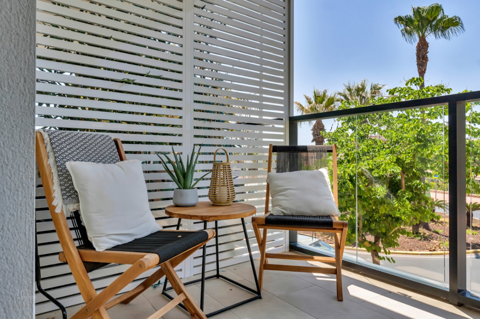 Private Terrasse mit Holzklappstühlen, weißem Sichtschutz und Glasgeländer mit Blick auf die umliegenden Palmen und Grünanlagen.