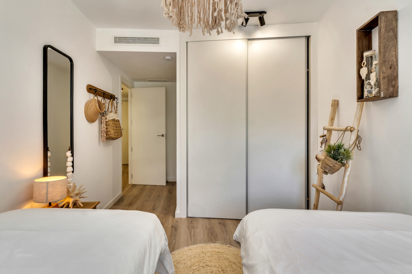 Schlafzimmer mit zwei Einzelbetten, weißem Einbauschrank mit Schiebetüren und mediterraner Dekoration auf hochwertigem Laminatboden in hellem Design.