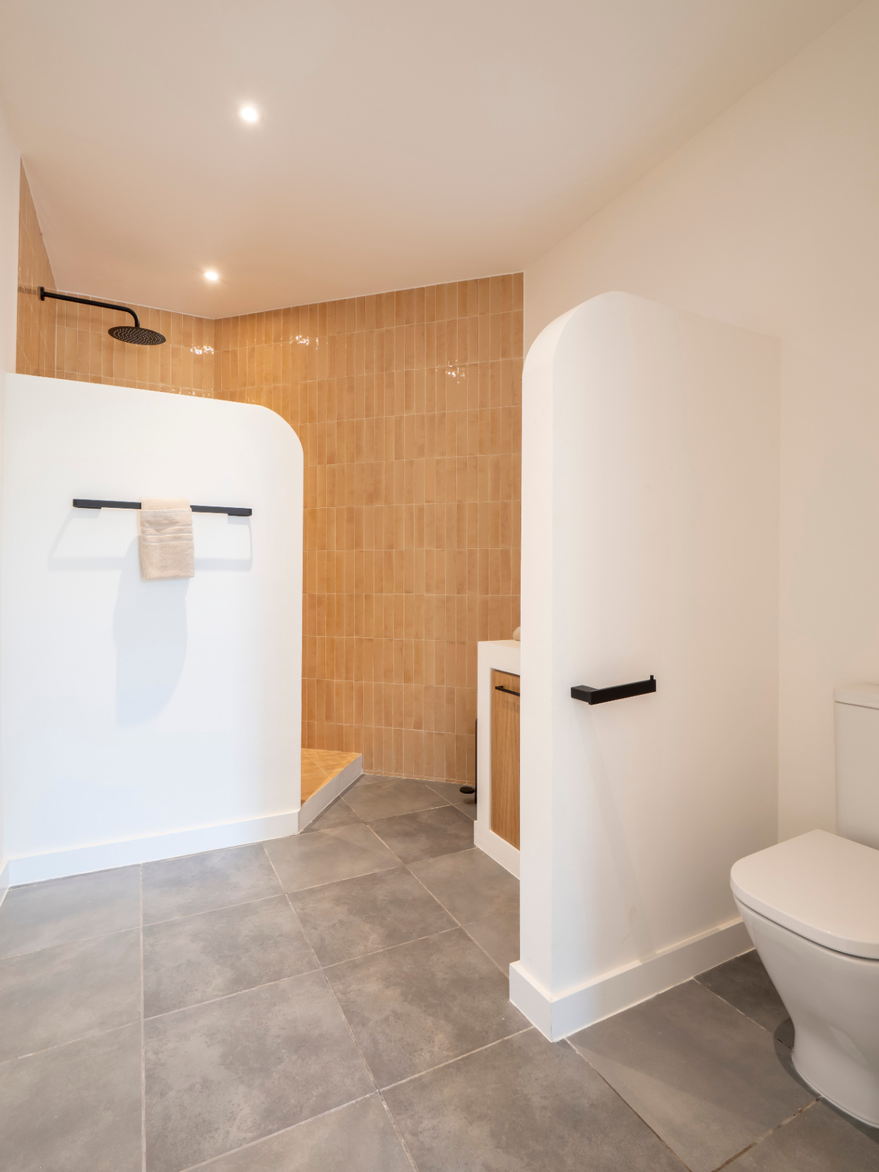 Badezimmer mit ebenerdiger Dusche und ockerfarbenen Fliesen. Waschtisch aus Holz und grauer Fliesenboden.