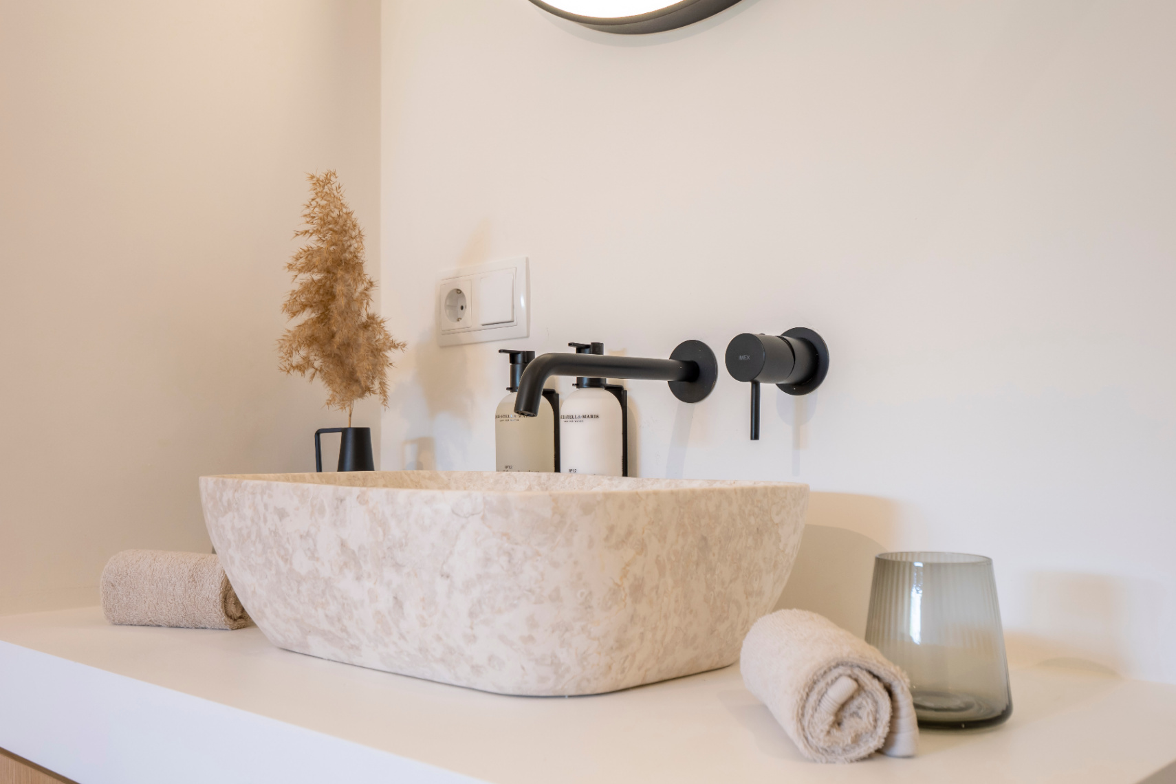 Badezimmerdetail mit Natursteinwaschbecken und mattschwarzen Armaturen. Minimalistisches Dekor mit passenden Handtüchern.