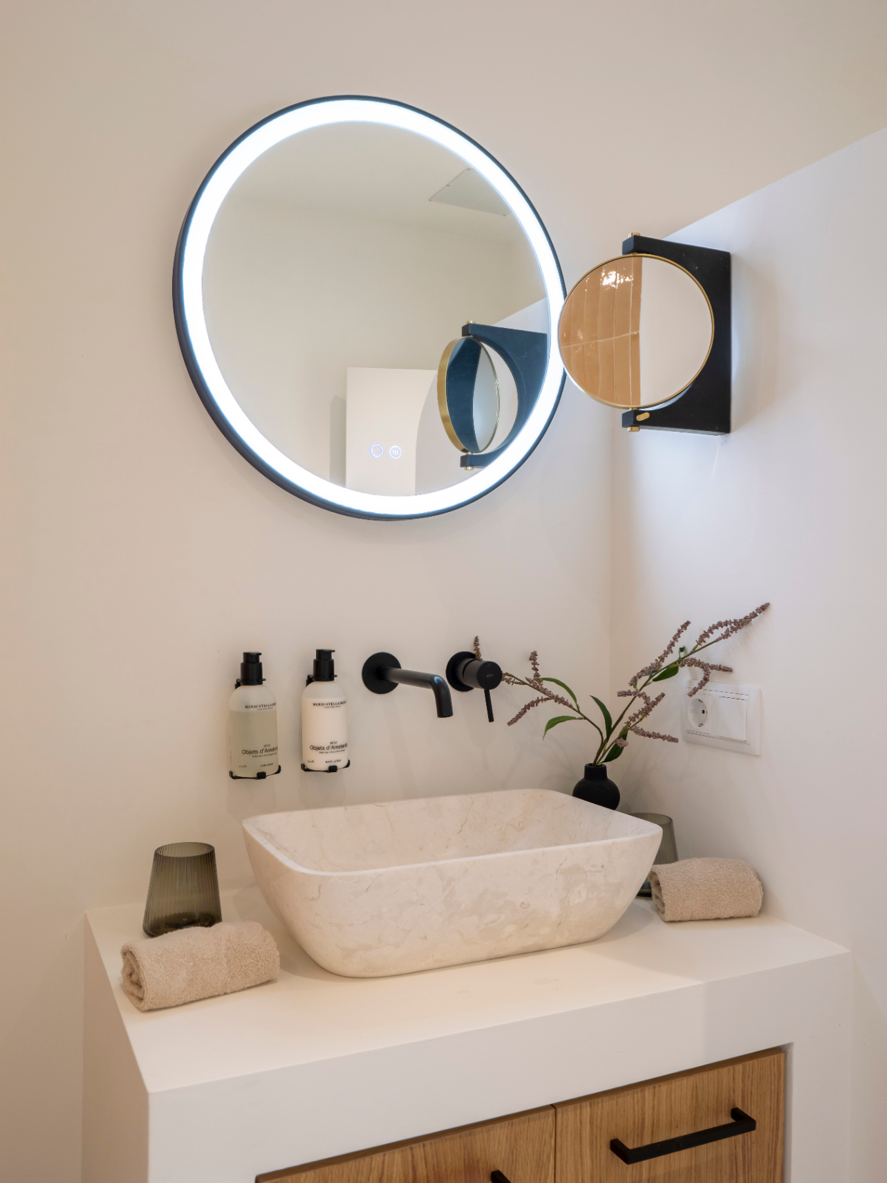 Badezimmerdetail mit Steinwaschbecken, mattschwarzen Armaturen und LED-beleuchtetem Spiegel.