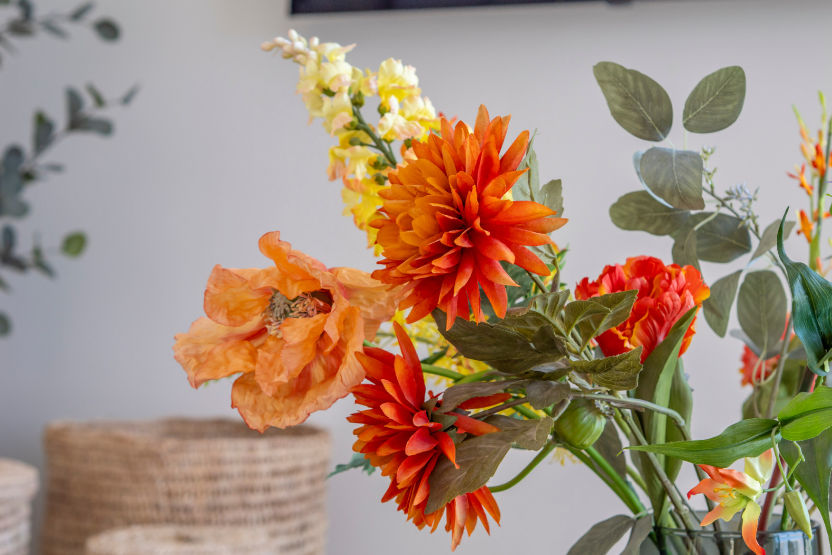 Blumendetail mit orangefarbener Dahlie und Mohn in einer Vase, das dem Interieur einen Hauch von Farbe verleiht.