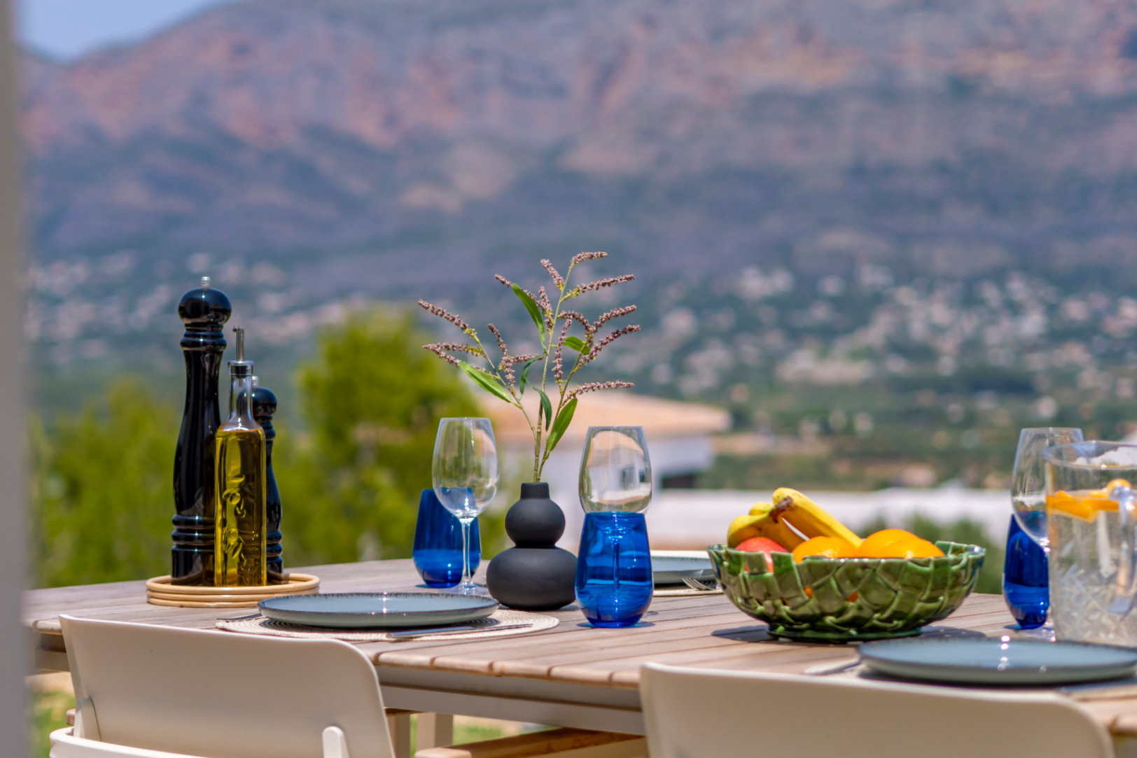 Essbereich im Freien mit Bergblick. Holztisch mit blauem Geschirr und Obstschale. Mediterranes Ambiente.