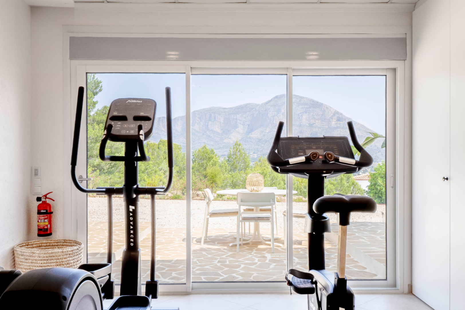Heller Fitnessraum mit Bergblick, ausgestattet mit Heimtrainer und Ellipsentrainer.