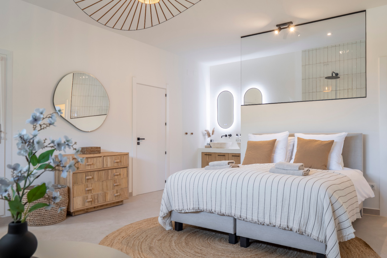 Helles Schlafzimmer mit integriertem Bad. Steinwaschbecken und hinterleuchteter Spiegel.