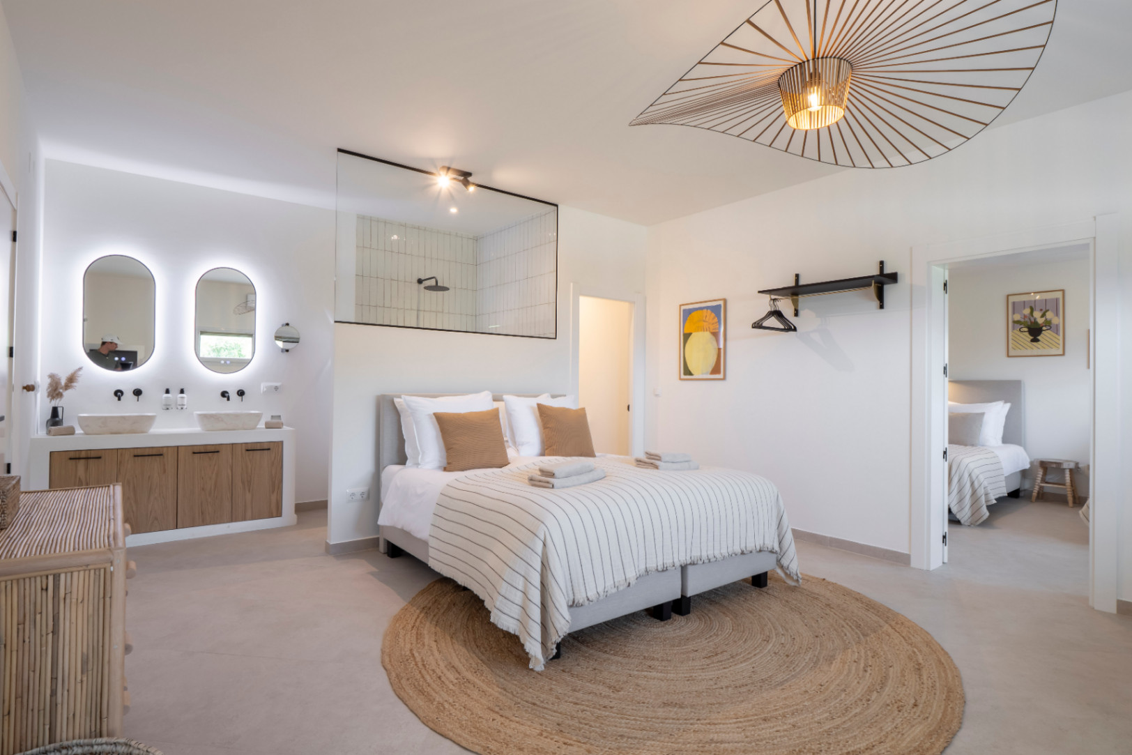 Helles Schlafzimmer mit integriertem Bad und Doppelwaschbecken mit hinterleuchteten Spiegeln.