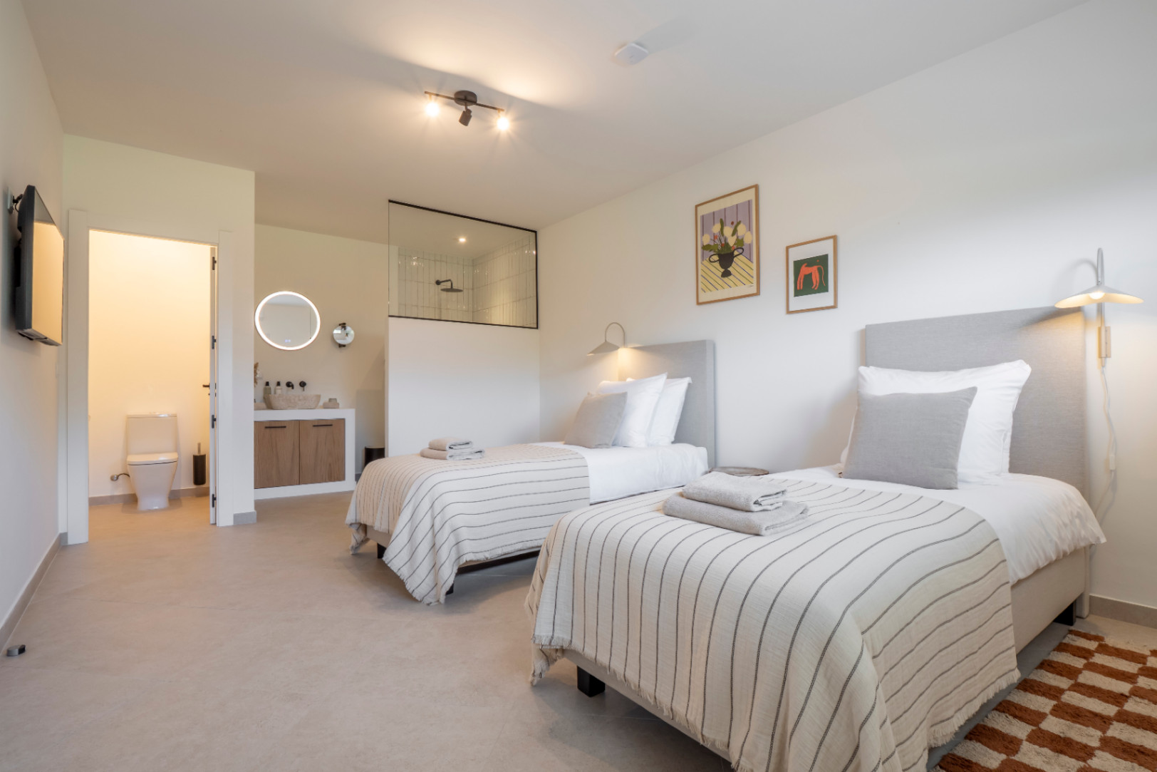 Helles Schlafzimmer mit zwei Einzelbetten, Bad en Suite mit verglaster Dusche und Waschtisch aus hellem Holz.
