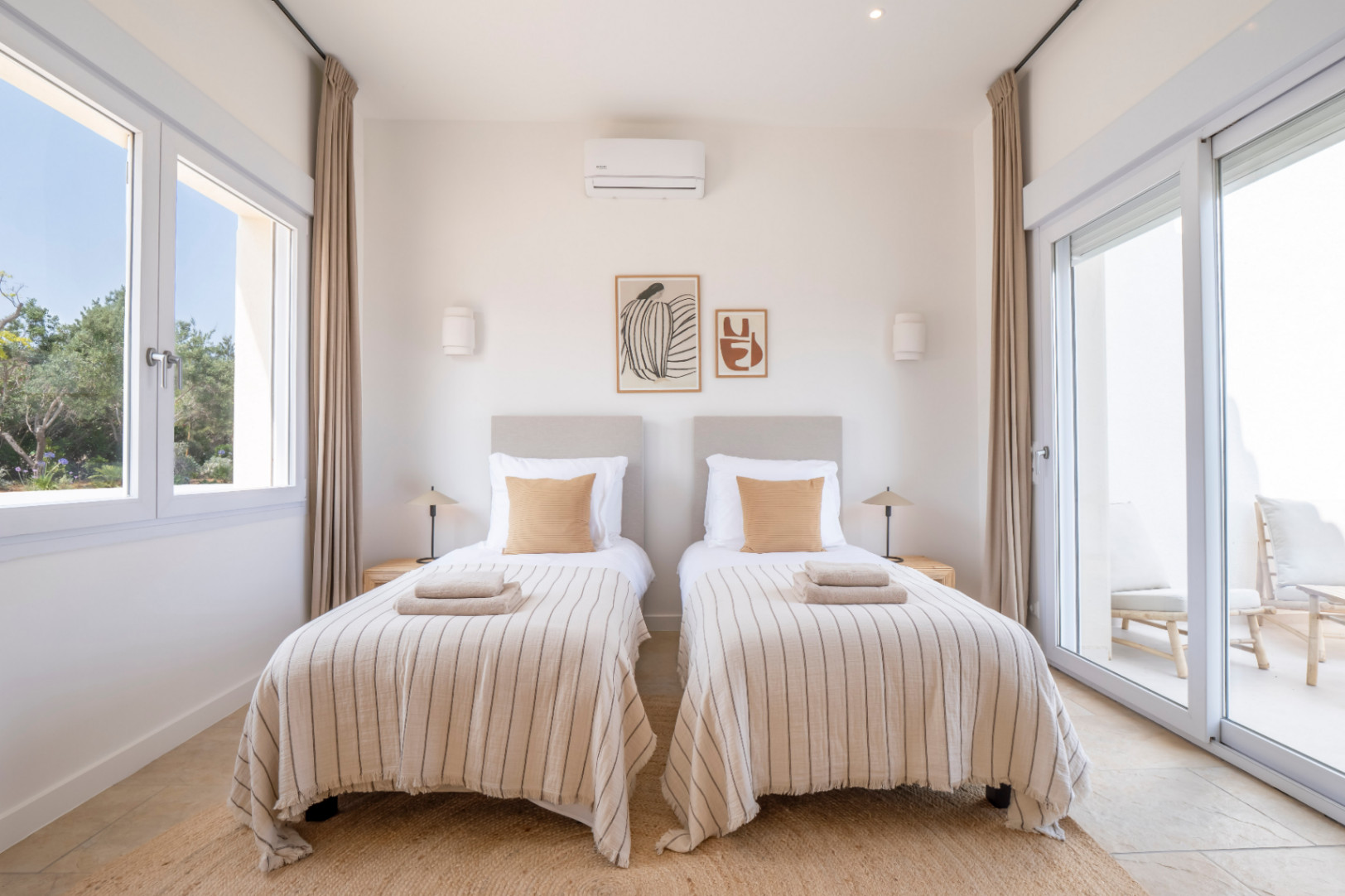 Helles Schlafzimmer mit zwei Einzelbetten, gestreifter Bettwäsche und minimalistischem Dekor. Zugang zu einer Außenterrasse.