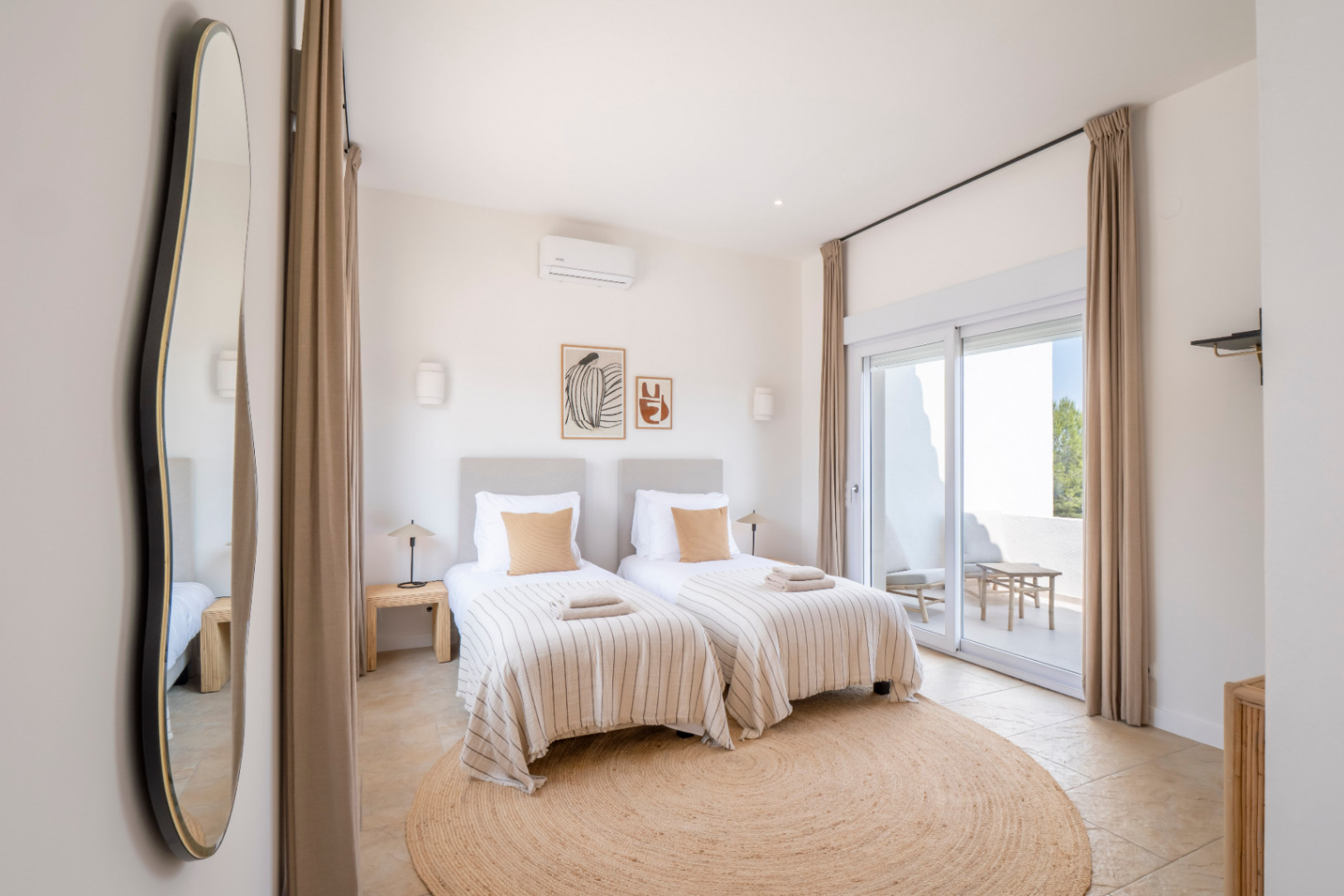 Helles Schlafzimmer mit zwei Einzelbetten, rundem Jute-Teppich und Zugang zur Außenterrasse.