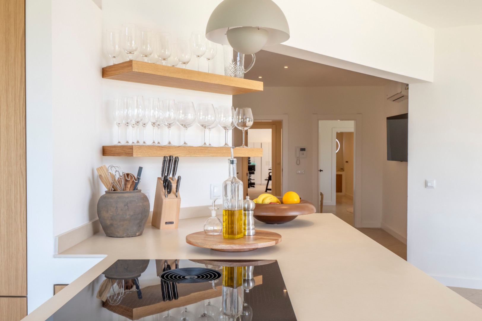 Küchendetail: Helle Holzregale mit Gläsern, beige Arbeitsplatte mit Induktionskochfeld und minimalistischem Dekor.
