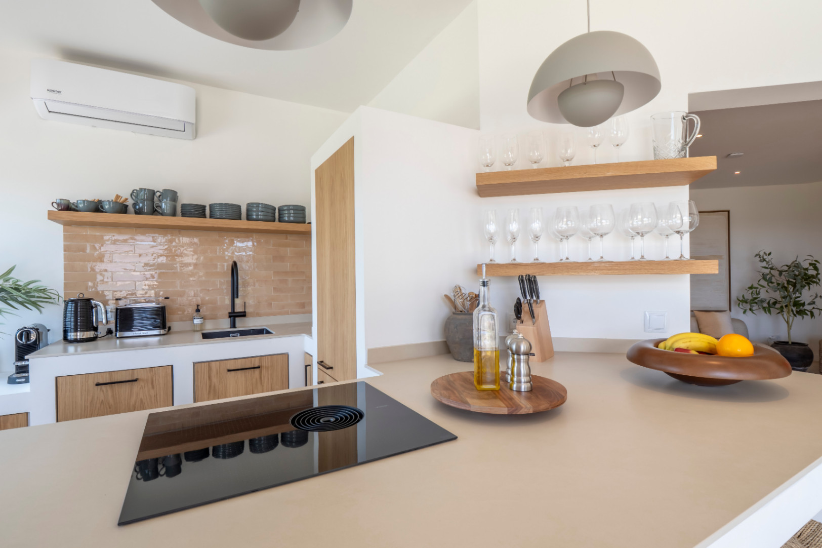 Küchendetail mit beiger Arbeitsplatte, schwarzem Glaskeramikkochfeld und hellen Holzregalen mit Gläsern.