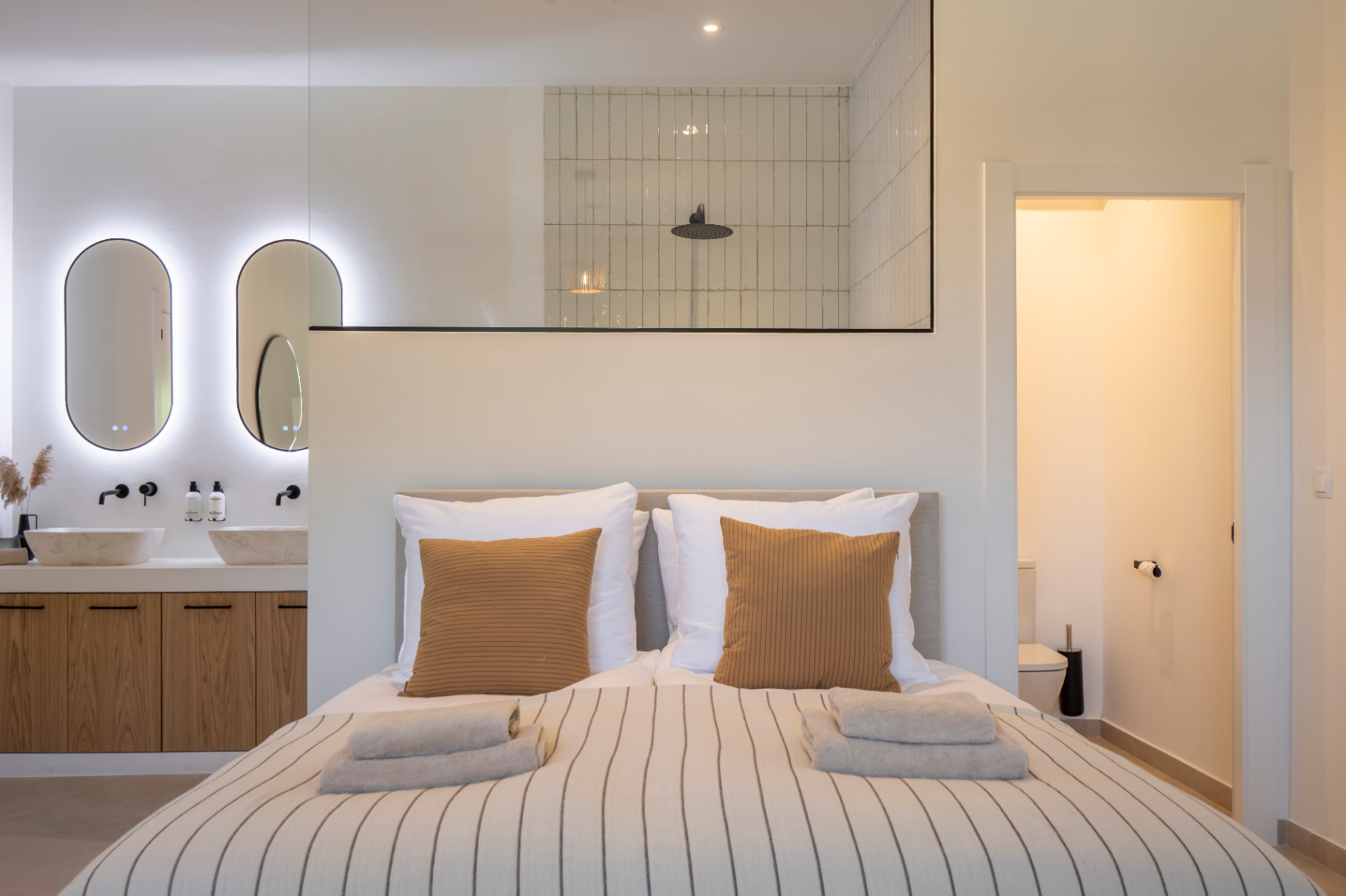 Schlafzimmer mit Bad en suite. Steinwaschbecken auf hellem Holzschrank und LED-Beleuchtung.