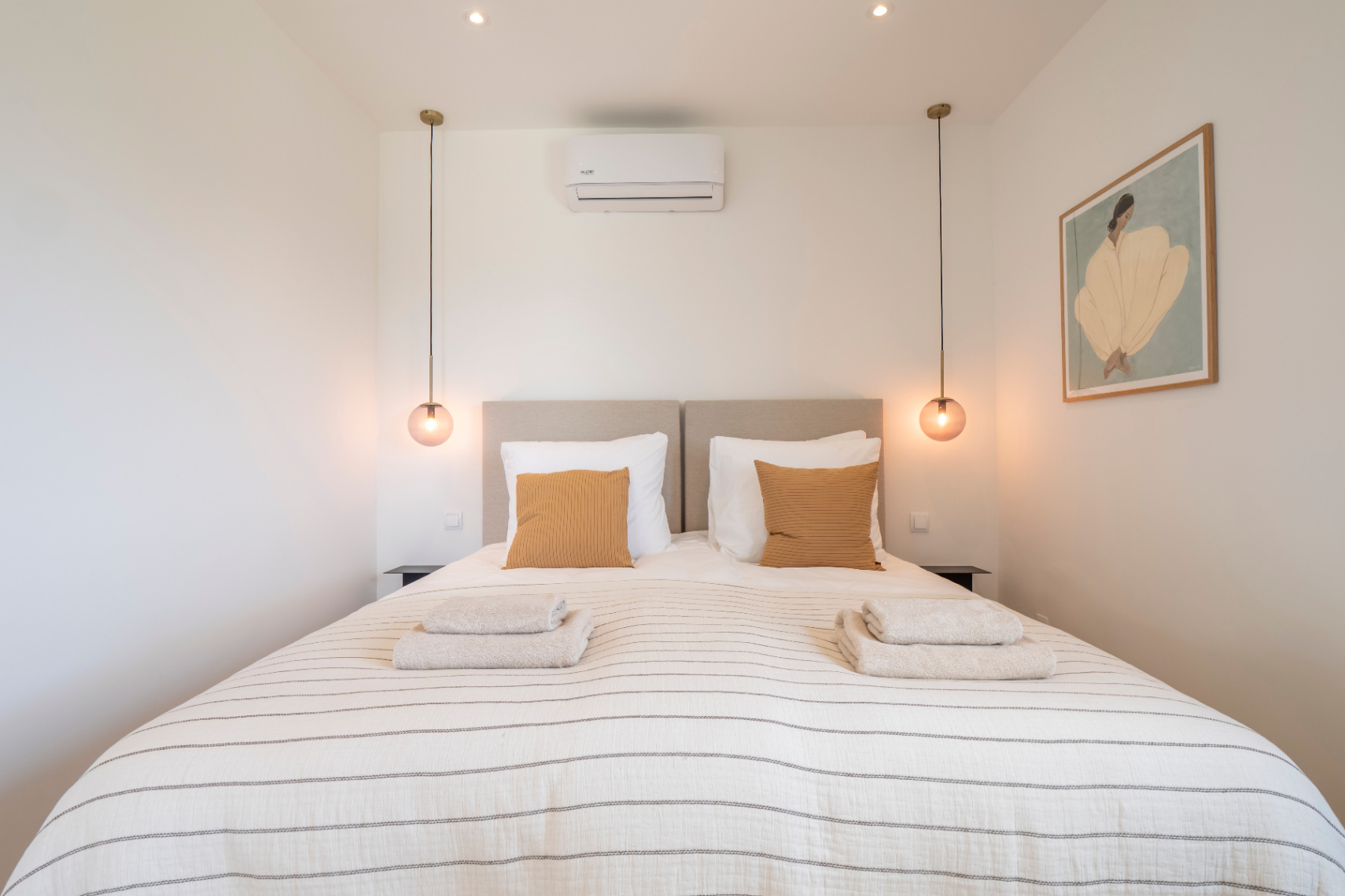 Schlafzimmer mit Doppelbett, gestreifter Bettwäsche und kugelförmigen Pendelleuchten.
