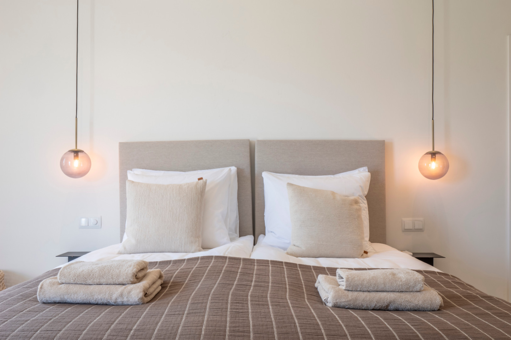 Schlafzimmer mit Einzelbetten, gepolsterten Kopfteilen und bernsteinfarbenen Glaspendelleuchten.