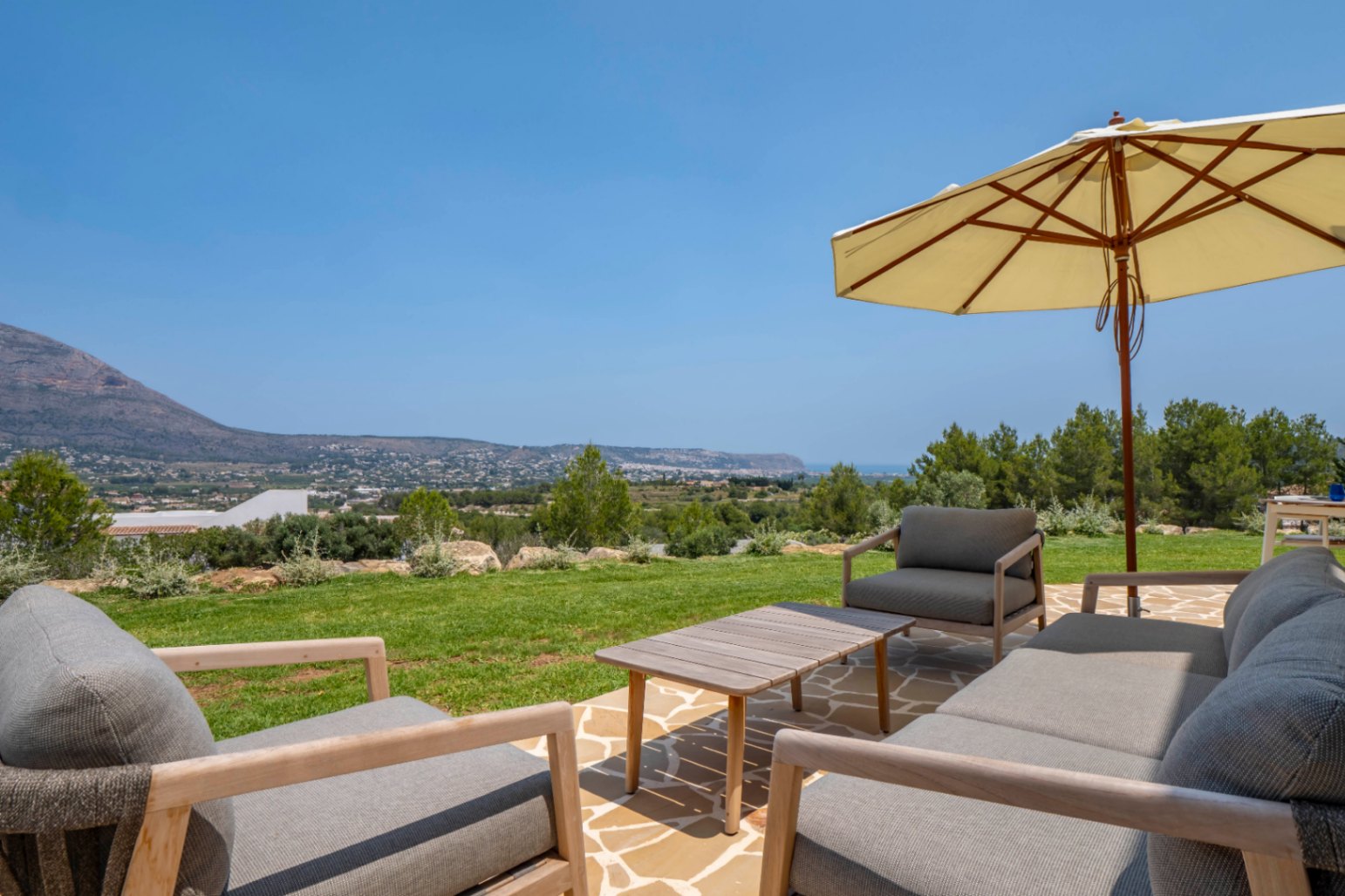 Terrasse mit Aussicht: Stein- und Holzgartenmöbel unter Sonnenschirm, mit Blick auf Jávea.
