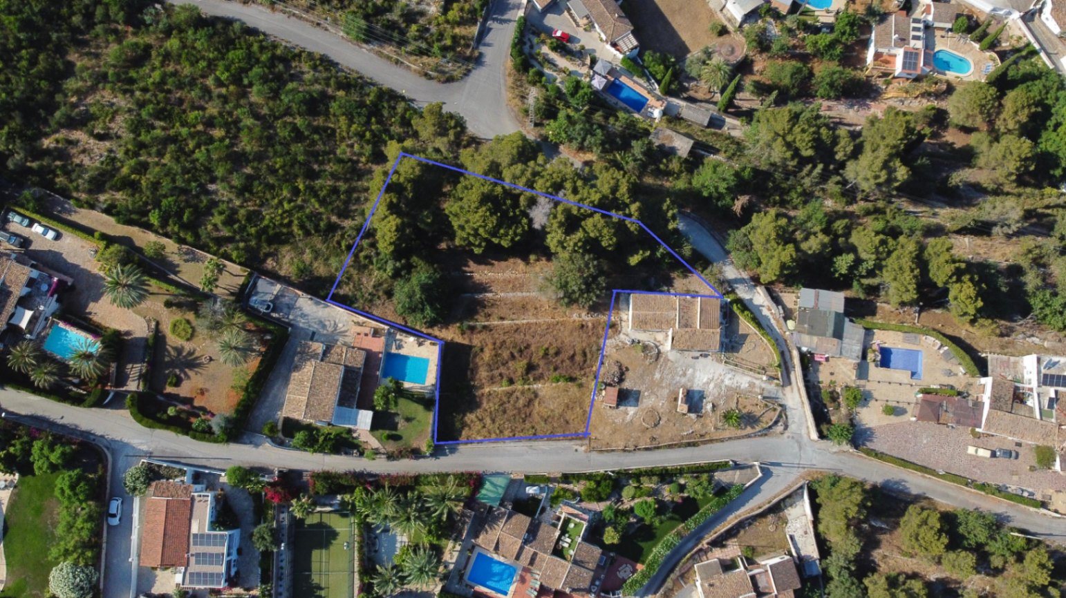 Luftaufnahme des 1.908 m² großen Grundstücks in Jávea mit blauer Umrandung, terrassiertem Gelände und Baumbestand in einer etablierten Wohngegend.