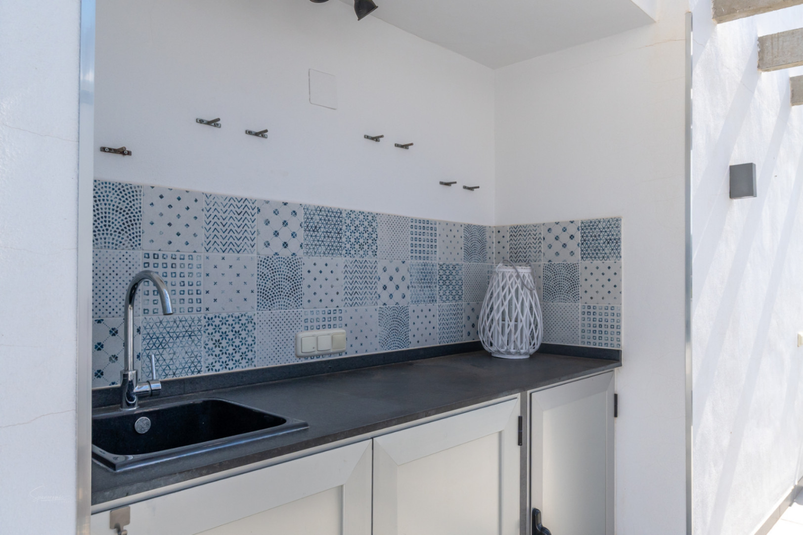 Außen-Sommerküche mit dunkler Arbeitsplatte, integrierter Spüle und einem dekorativen Fliesenspiegel mit blau-weißen Mustern.
