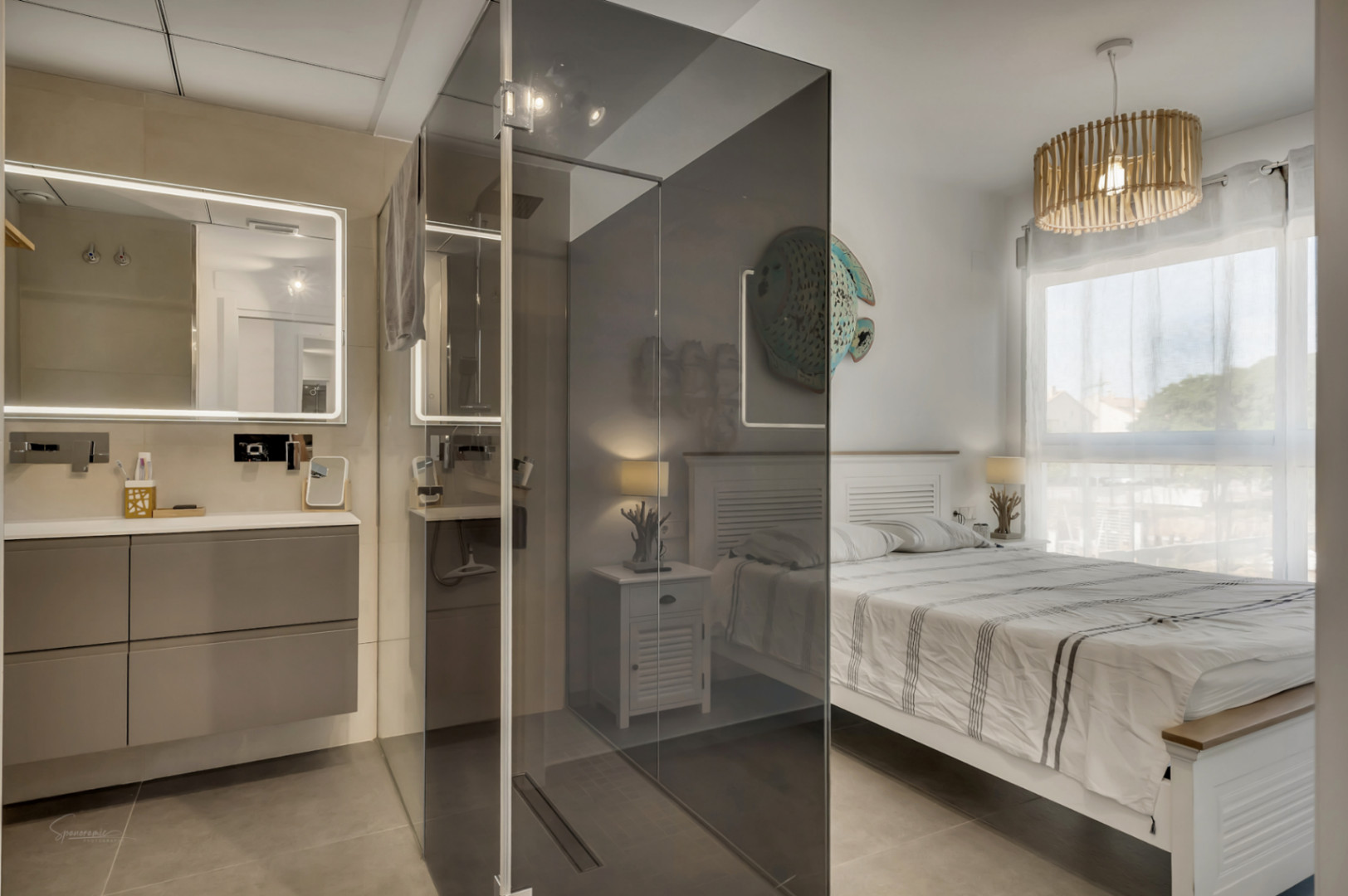 Hauptschlafzimmer mit integriertem Bad, ausgestattet mit einer begehbaren Dusche mit Rauchglaswand und einem schwebenden Waschtisch mit hinterleuchtetem Spiegel.