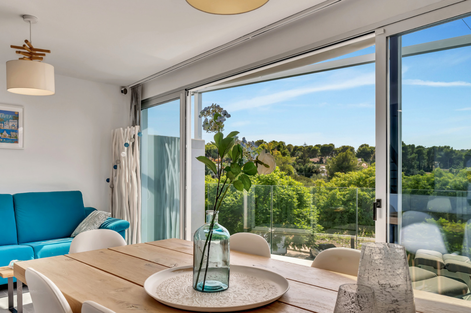 Heller Essbereich mit Holztisch und großen Glasschiebetüren, die einen weiten Blick auf die umliegende Landschaft und den Balkon mit Glasgeländer bieten.