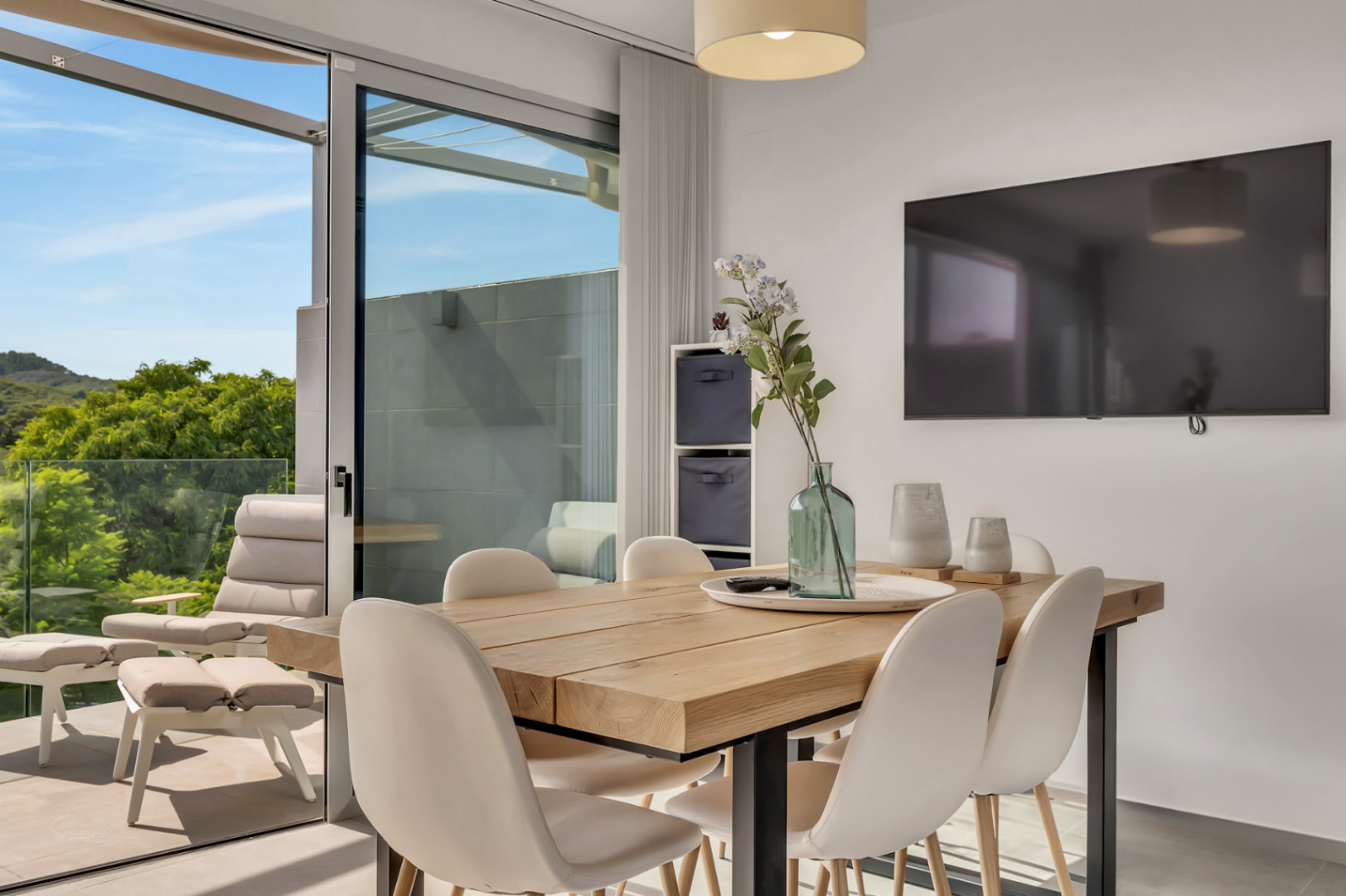 Heller Essbereich mit massivem Holztisch und direktem Zugang zum Balkon mit Glasgeländer und Blick auf die umliegende grüne Landschaft.